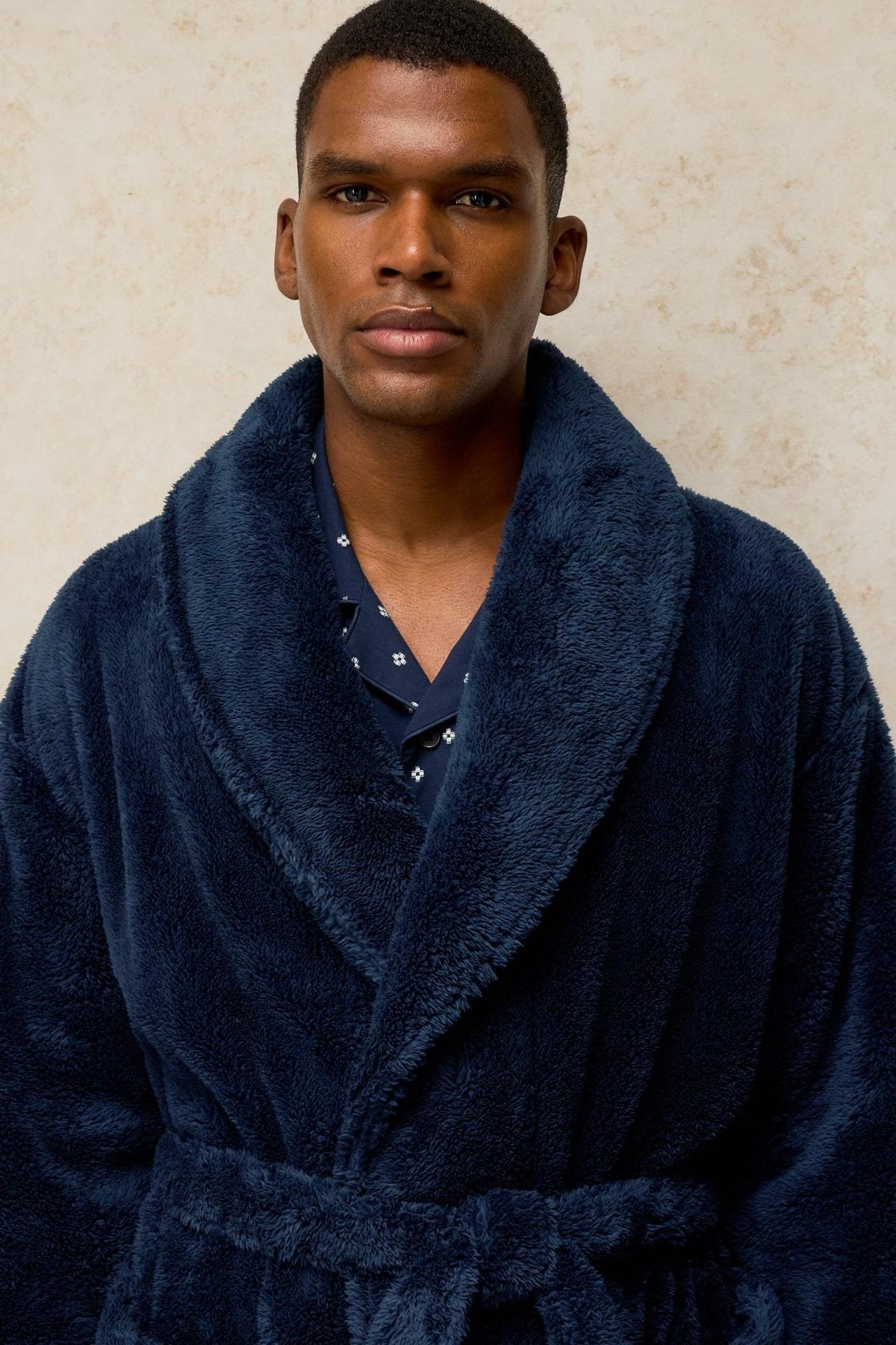 A man wearing a navy blue fluffy dressing gown over a patterned shirt, studio portrait.