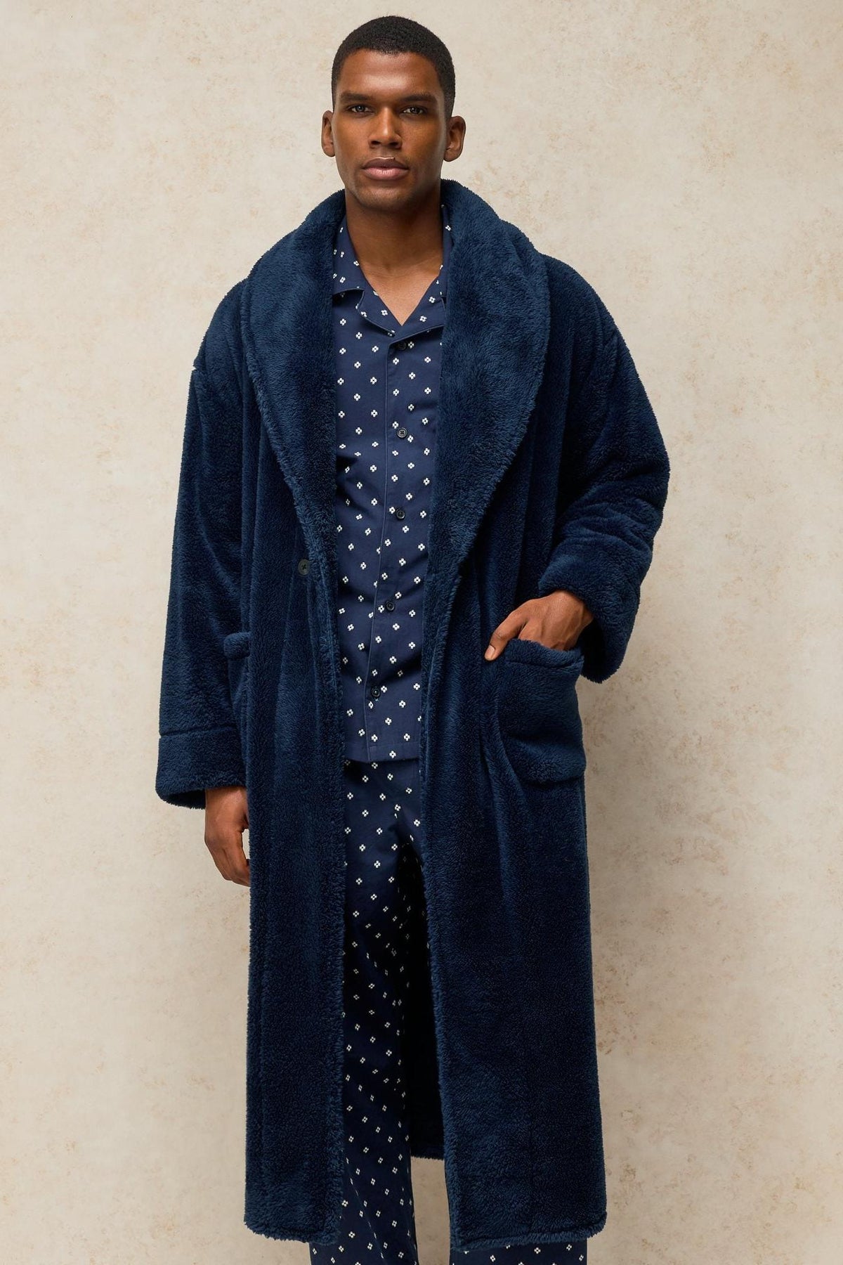 A man wearing a navy fluffy White Stuff dressing gown over matching patterned pyjamas against a neutral studio background.