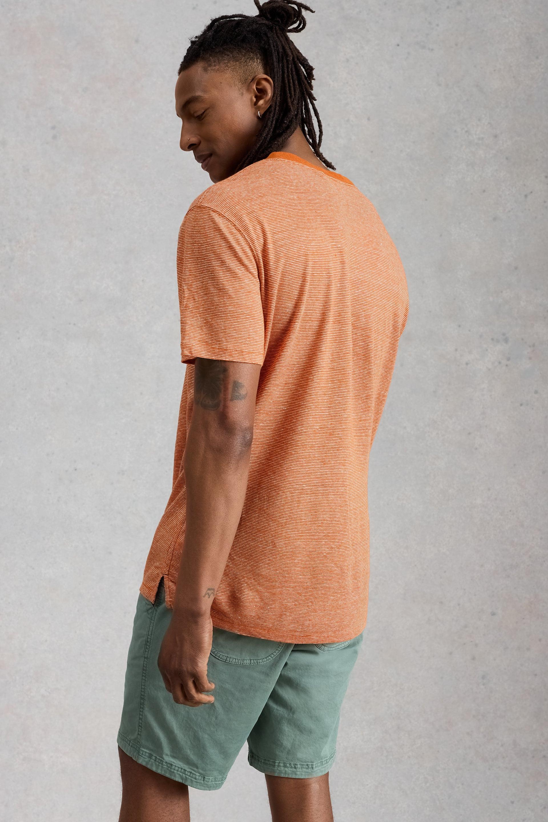 A man wearing an orange striped 100% linen t-shirt from behind against a neutral gray background.