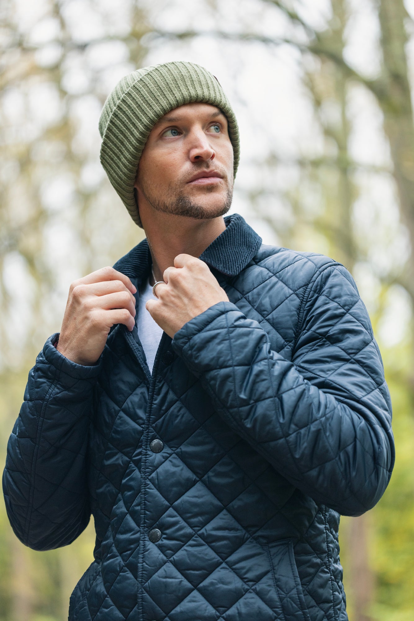 Man wearing a quilted jacket and knit beanie in a forest setting