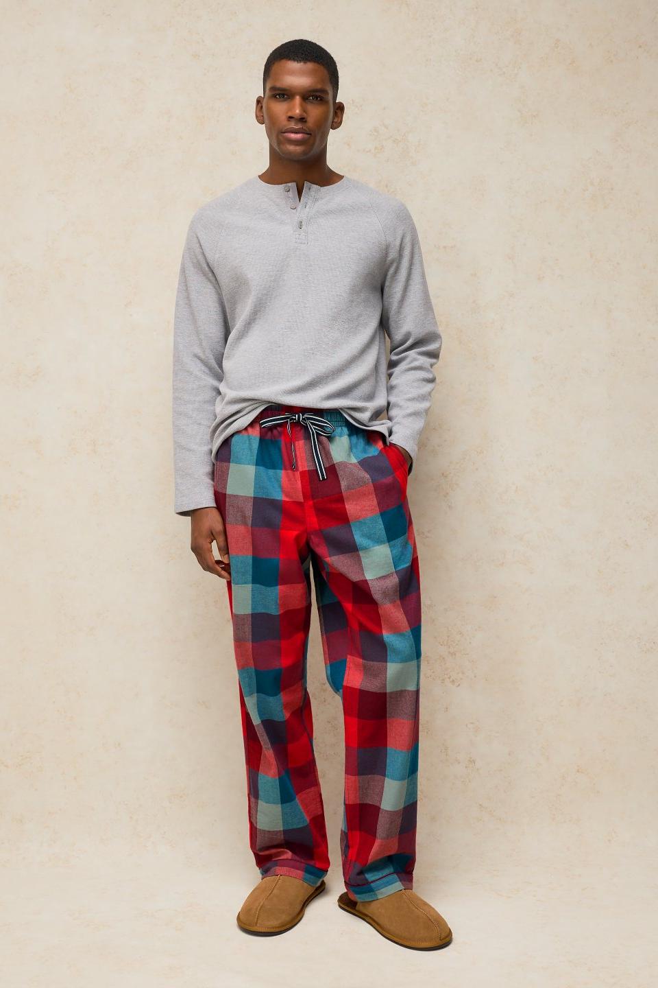 A man wearing a grey long-sleeve Henley top and red check organic cotton men's pyjamas against a neutral background.