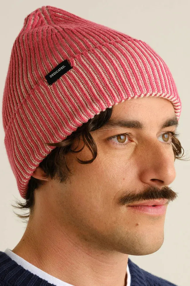 A man wearing a ribbed red Dedicated Clothing cotton beanie hat against a plain background.