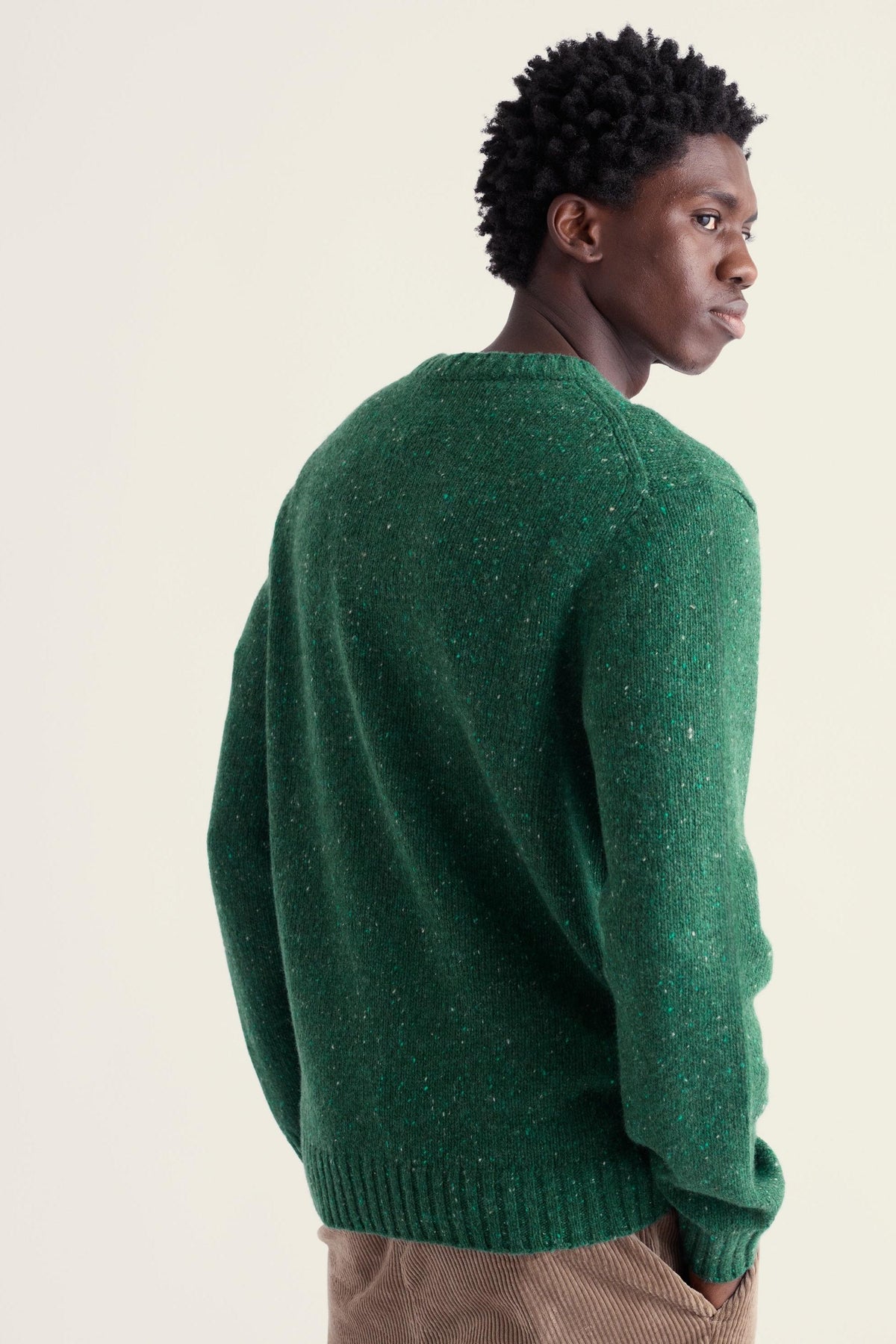 A man wearing a green Seasalt Cornwall merino wool sweater, viewed from behind and looking to the side.