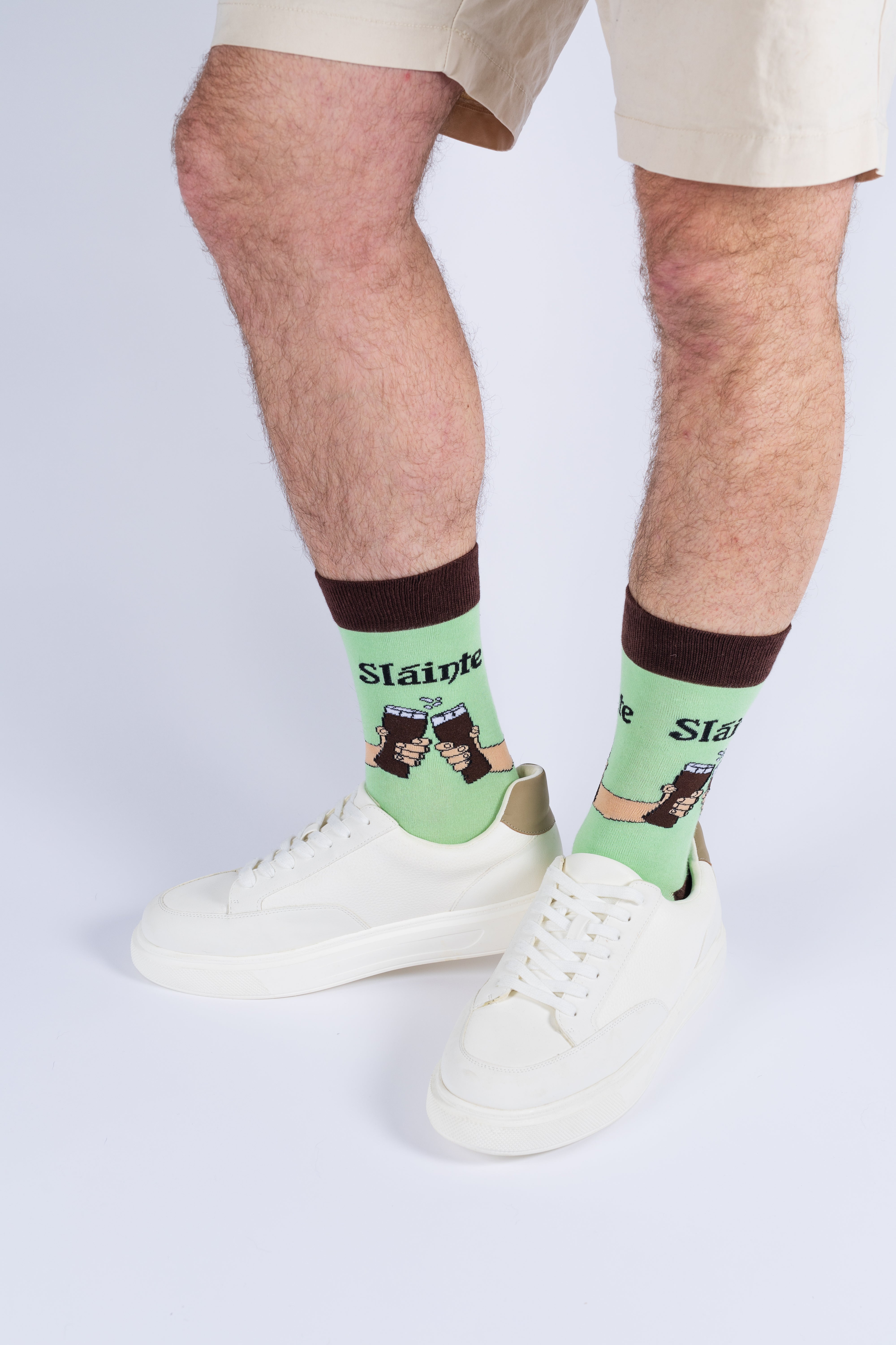 Close-up of a man wearing light green socks with a beer cheers print and white casual sneakers