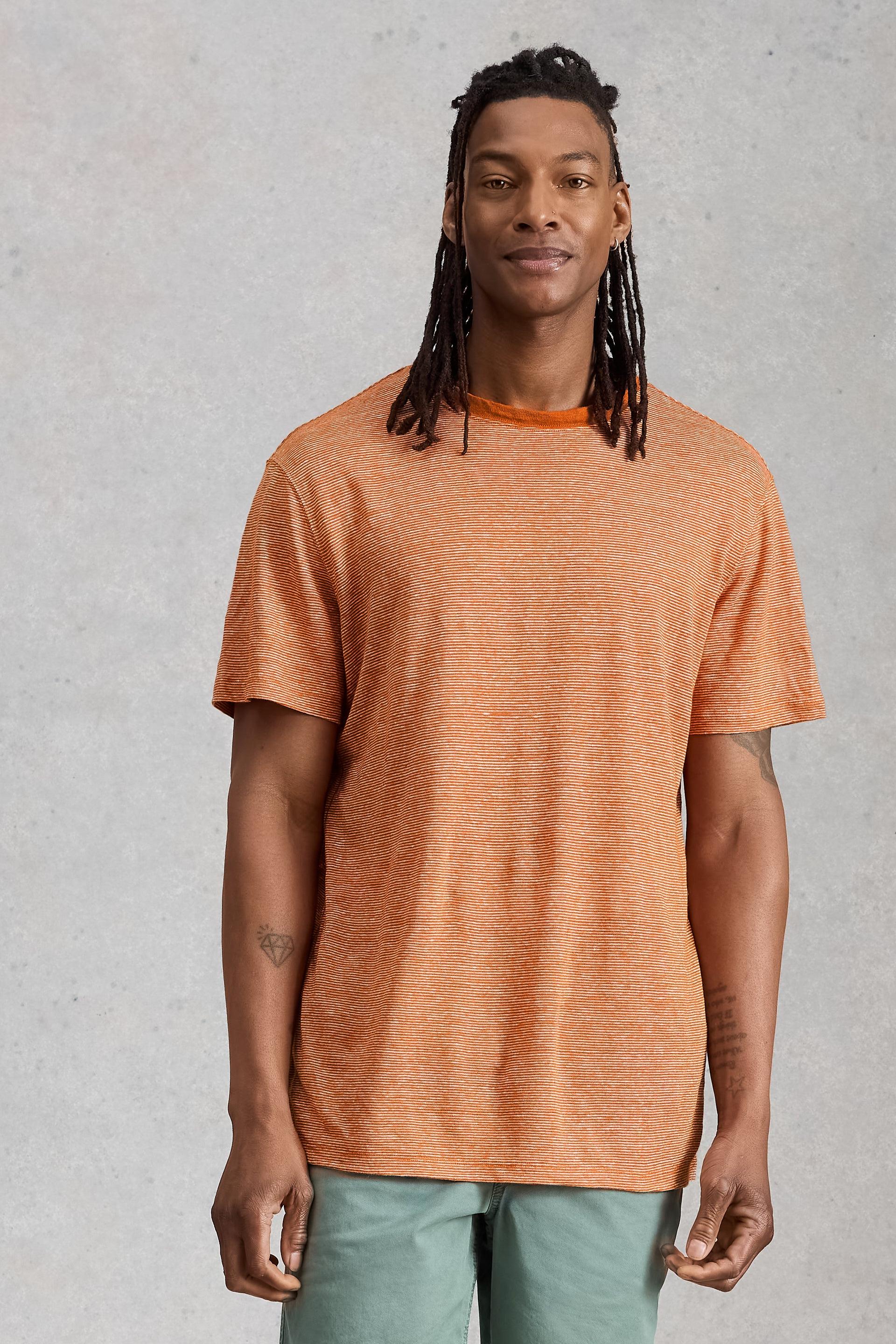 A man with dreadlocks wearing an orange striped 100% linen t-shirt against a grey background.