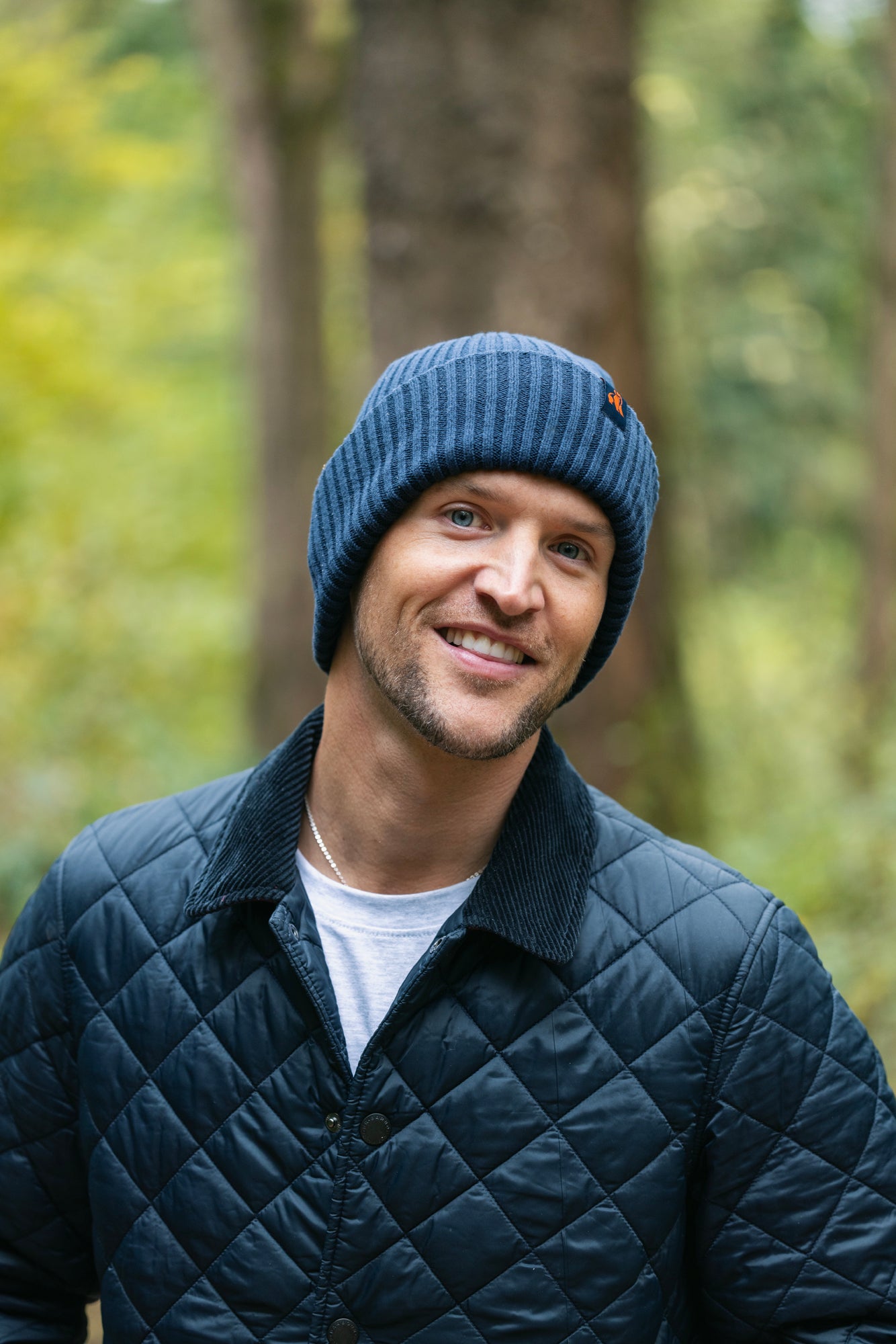 Smiling man wearing a blue Swole Panda beanie outdoors in a forest.