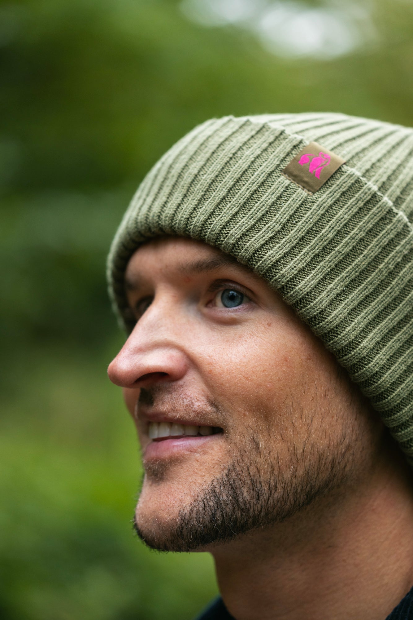 Man wearing a green beanie with a logo, looking to the side with a blurred green background