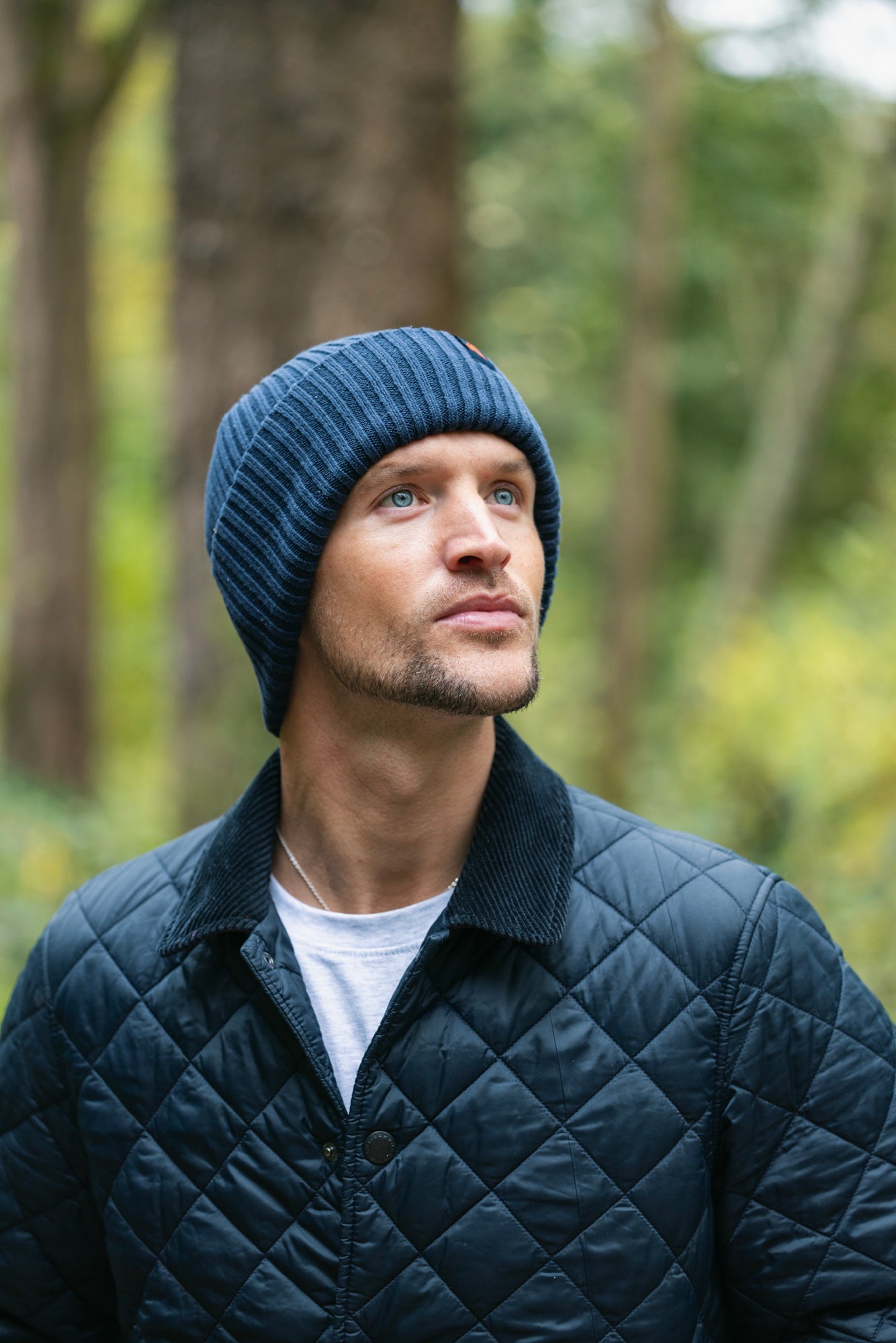 A man wearing a blue Swole Panda organic cotton beanie looking upwards in a forest setting.