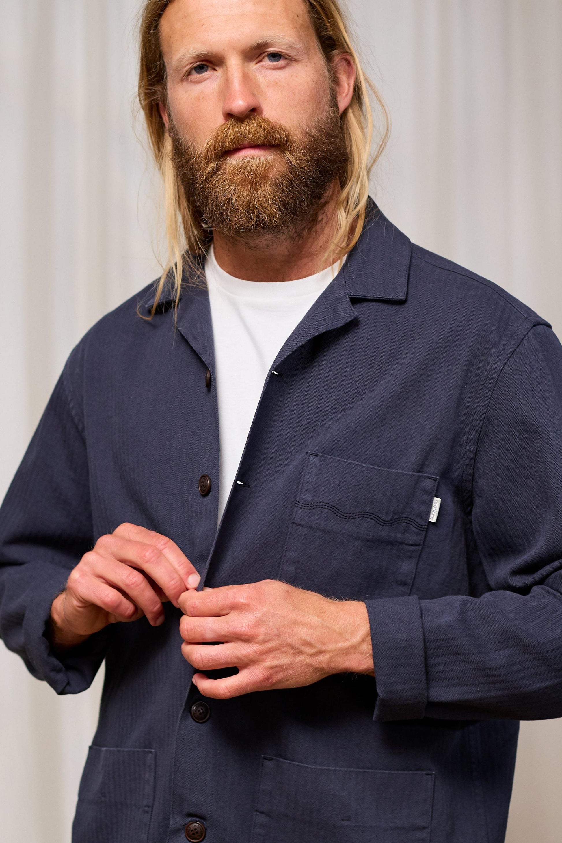 Man wearing a navy blue jacket over a white shirt against a plain background