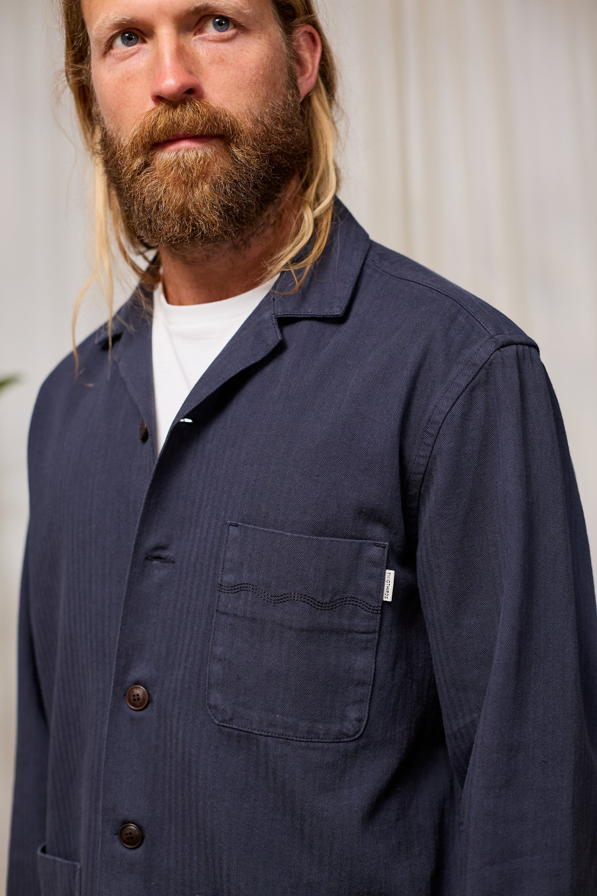 Man wearing a navy blue work jacket with a white shirt underneath against a neutral background
