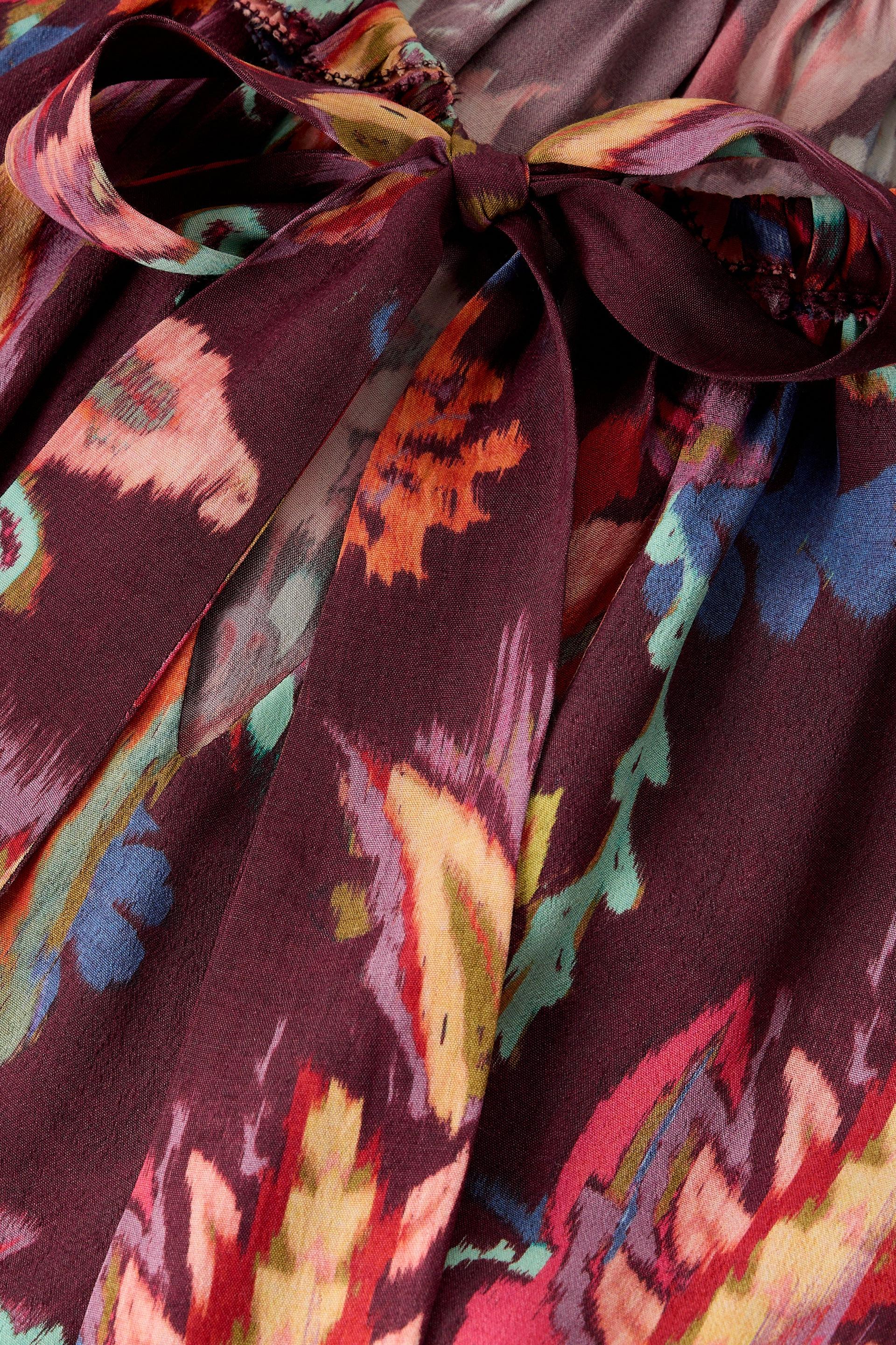 A close-up of a multicolor printed fabric with a large bow, featuring a deep burgundy base with abstract floral and ikat-like patterns in pink, orange, blue, green, and yellow.