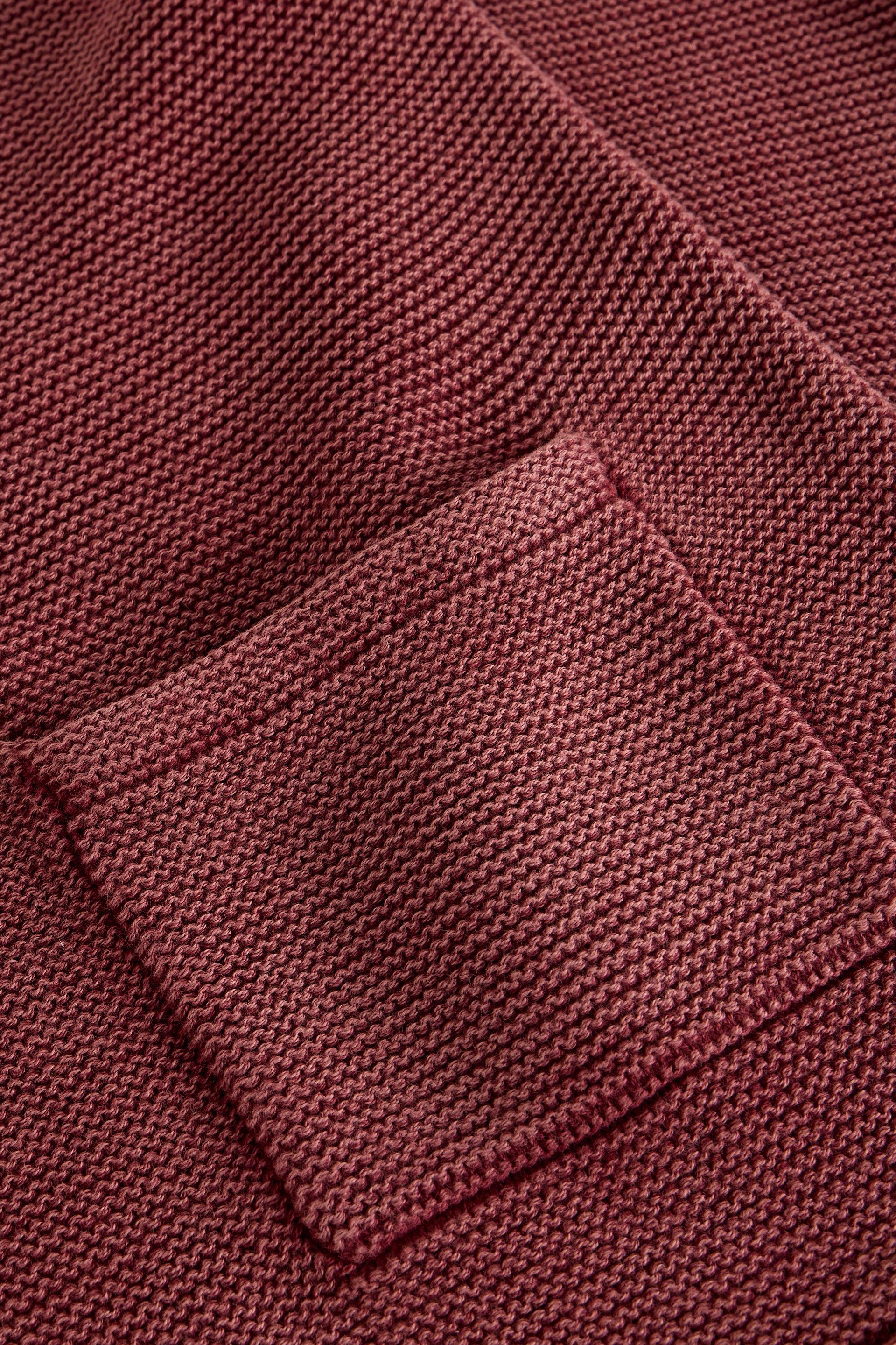 Close-up of a textured knit fabric in a muted burgundy or dusty rose tone, showing a pocket seam and fine woven detail.