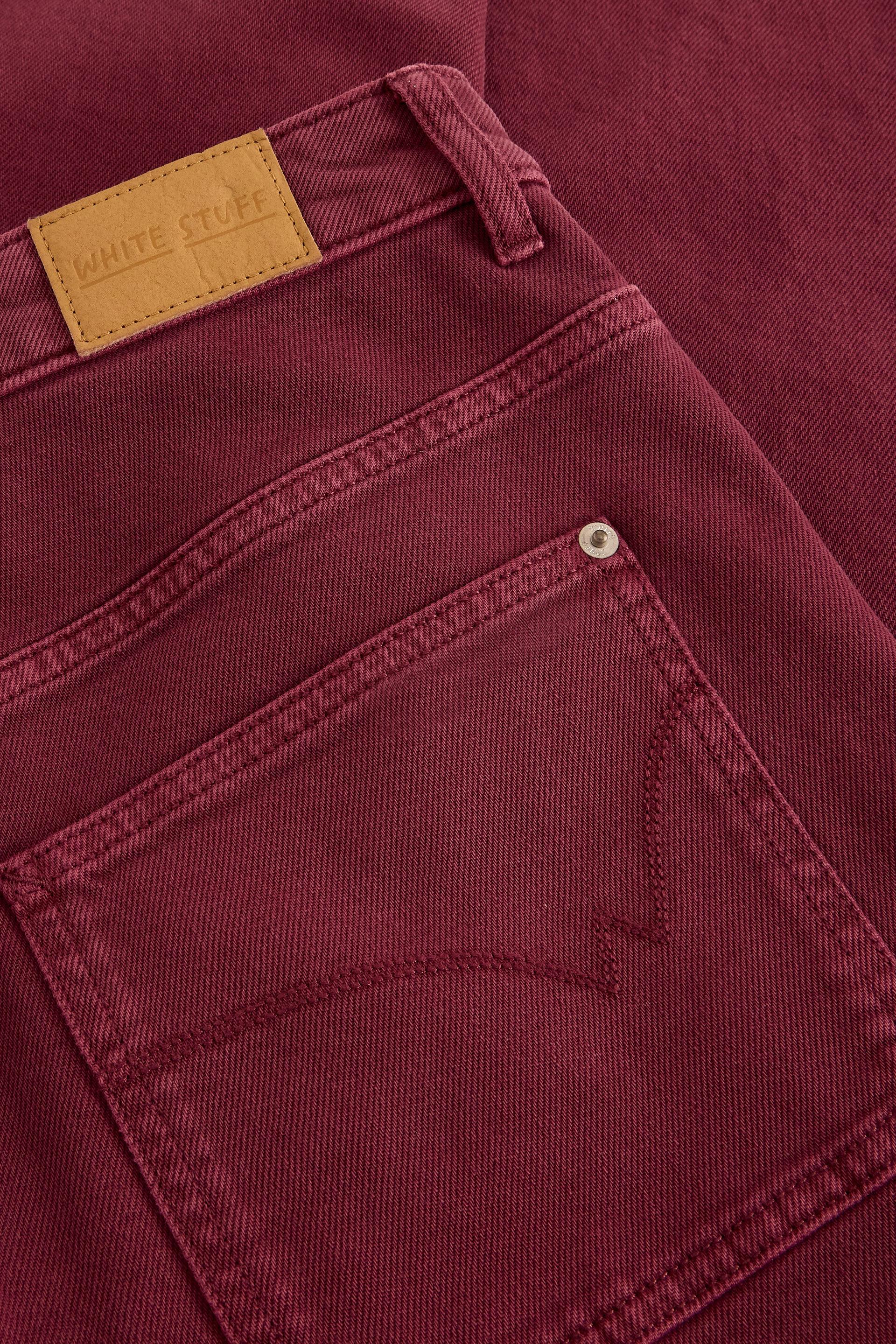 Close-up of maroon organic cotton jeans showing a White Stuff branded tan leather waist patch and back pocket.