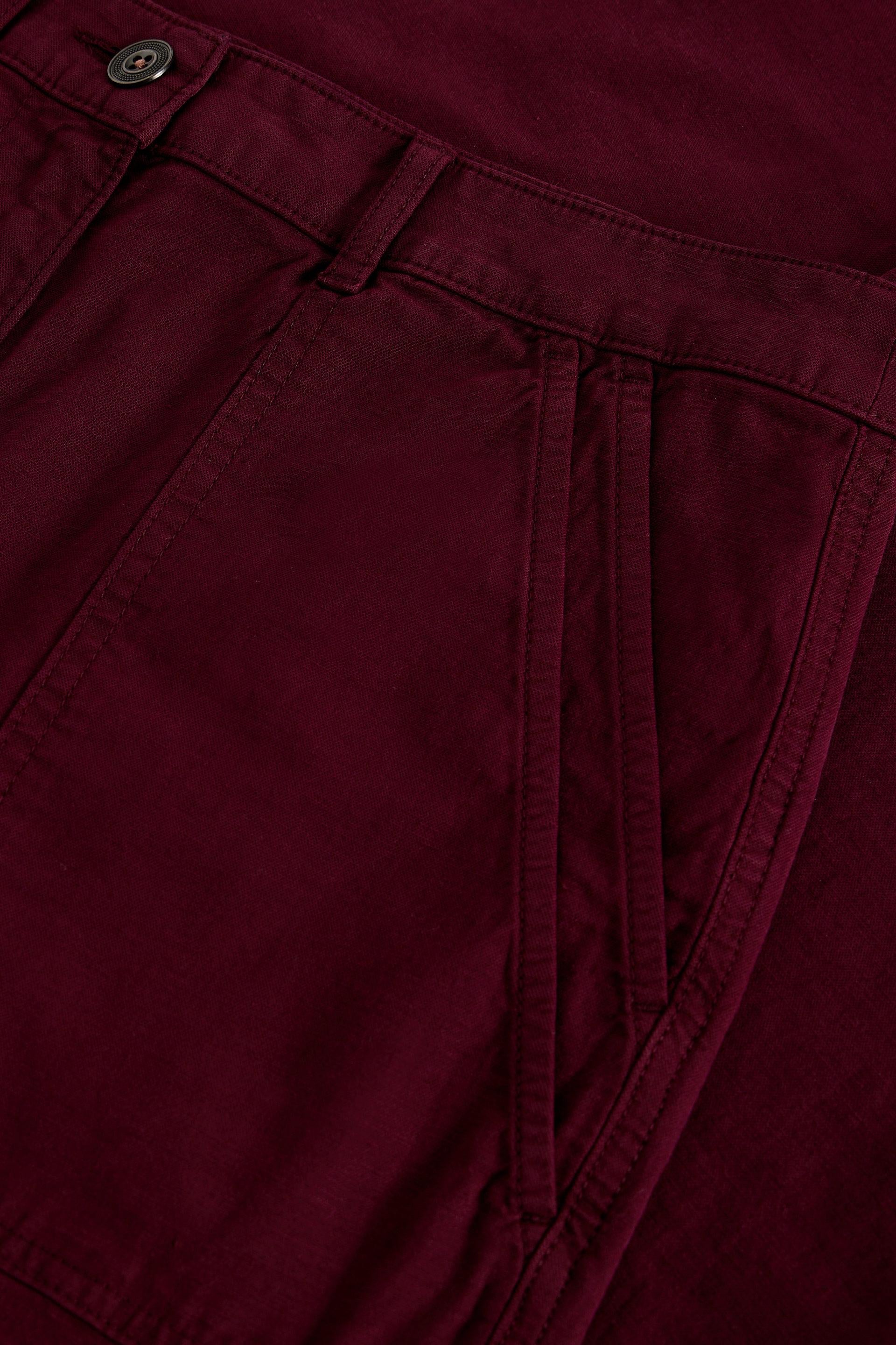 Close-up of maroon organic cotton trousers showing front pocket and button detail.