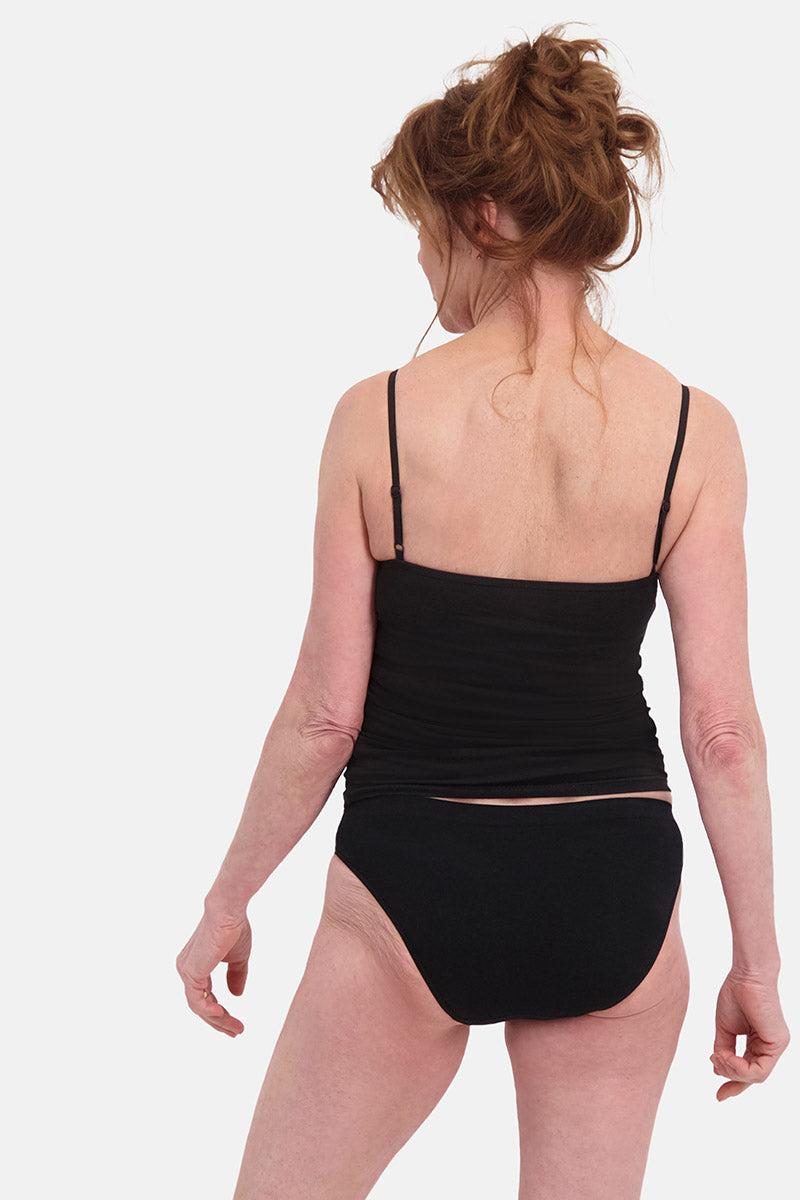 Rear view of a mature woman with auburn hair wearing a black camisole and matching briefs against a white background