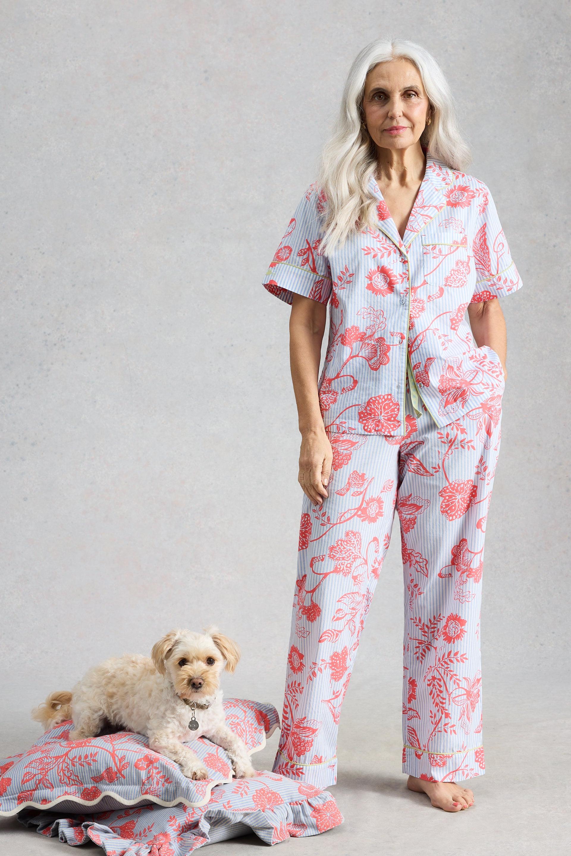 Mature woman with long silver hair wearing organic cotton pyjamas standing next to a small dog on a pillow.