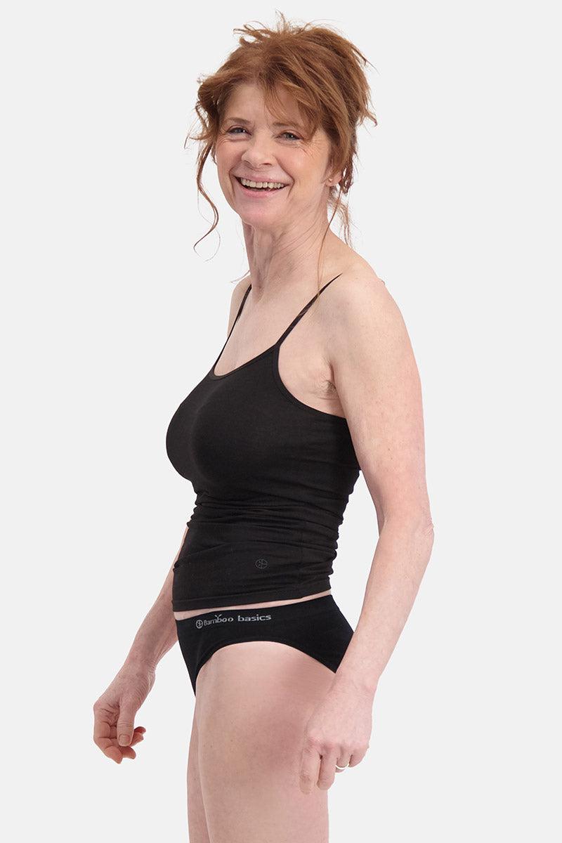 A smiling mature woman with auburn hair wearing a black tank top and Bamboo Basics underwear against a white background