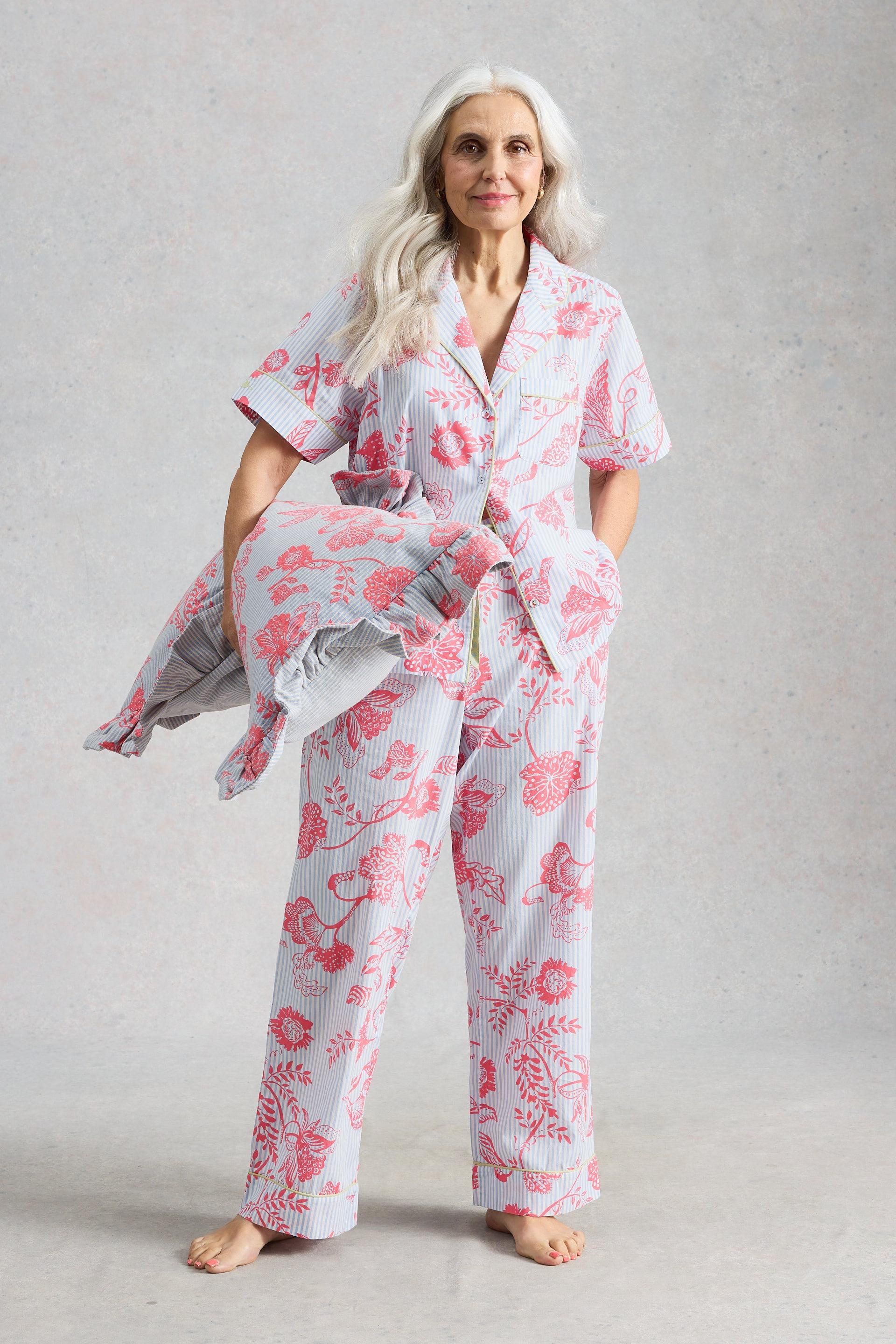 Mature woman with grey hair wearing floral patterned organic cotton pyjamas and holding a matching pillow.