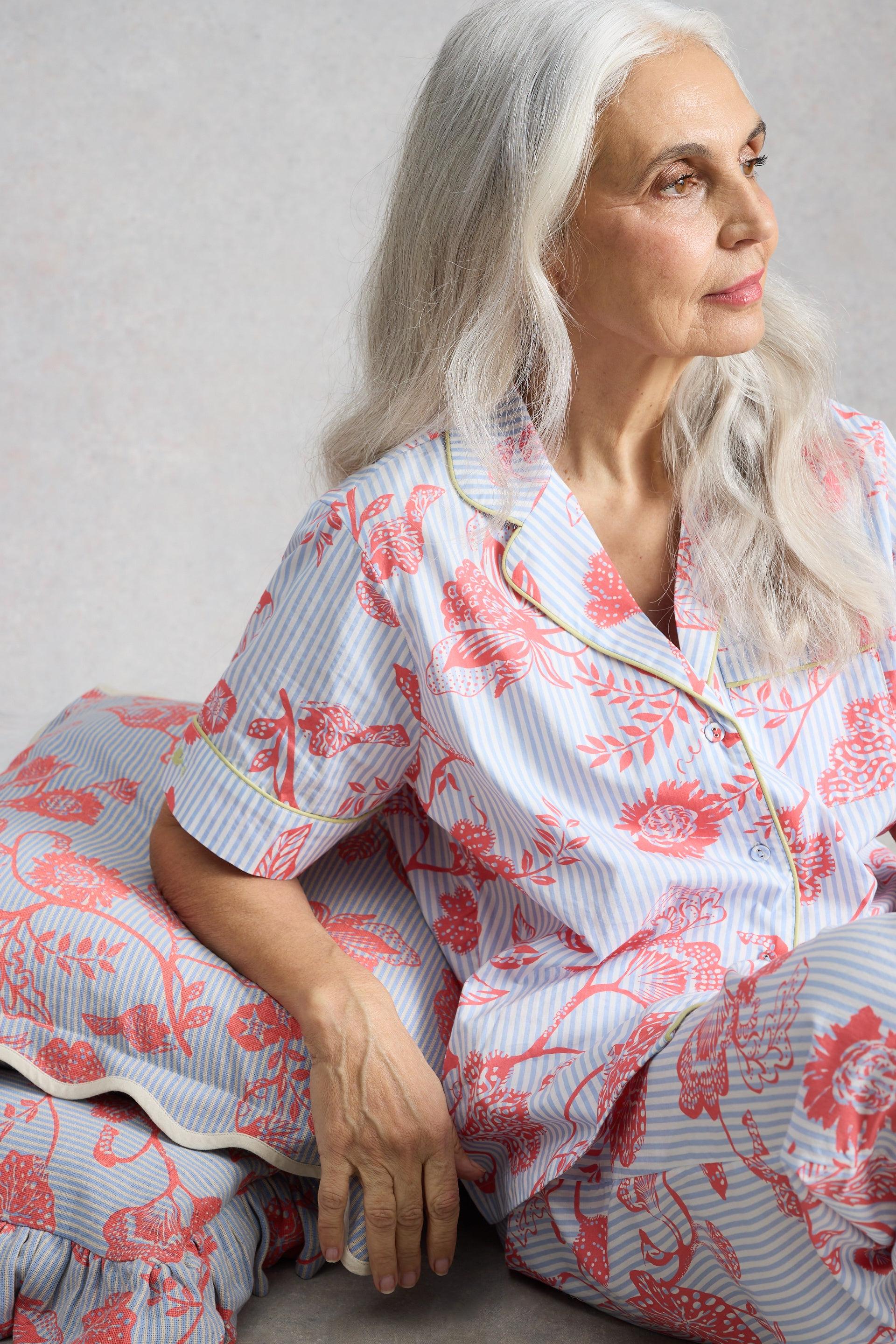 A silver-haired woman wearing a blue and coral patterned organic cotton pyjama set.