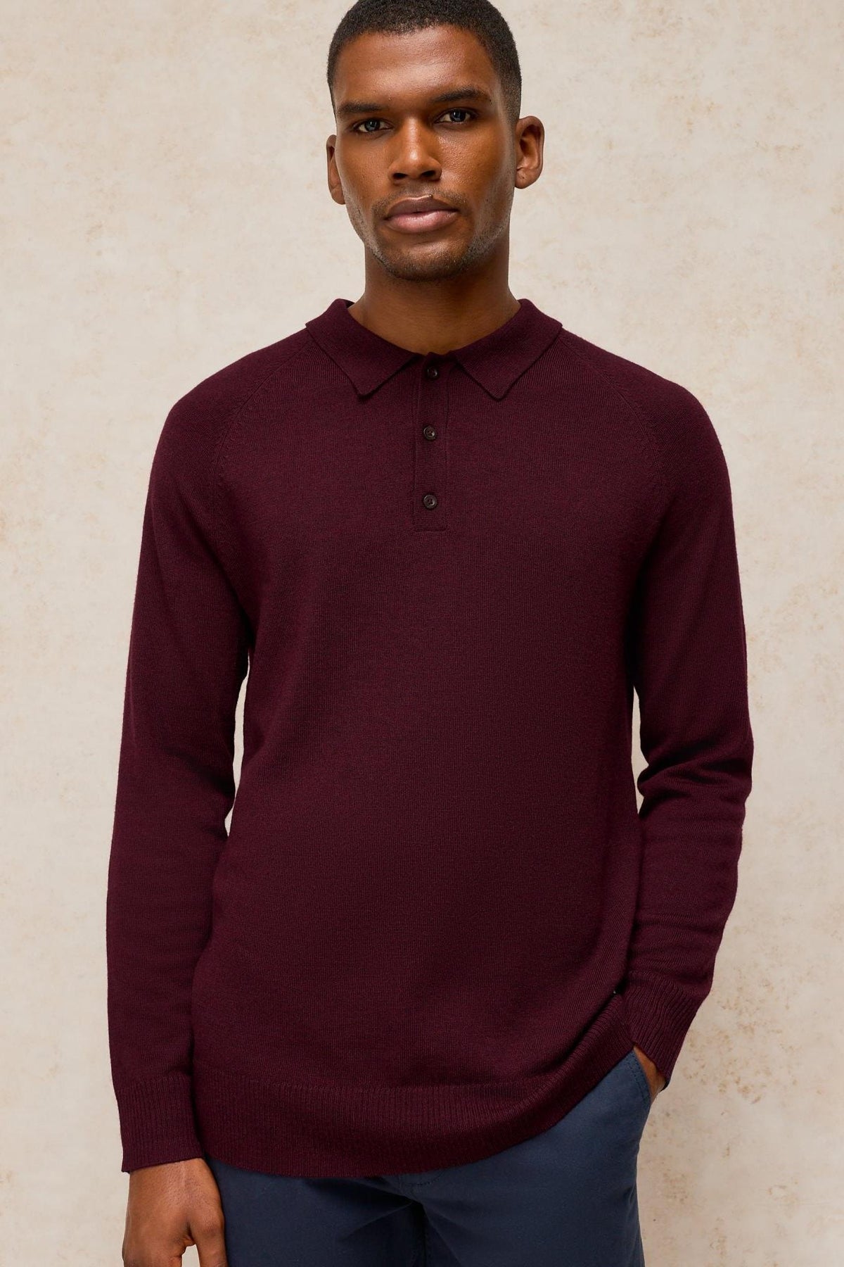 A man wearing a long-sleeved plum-coloured merino wool polo shirt against a neutral background.