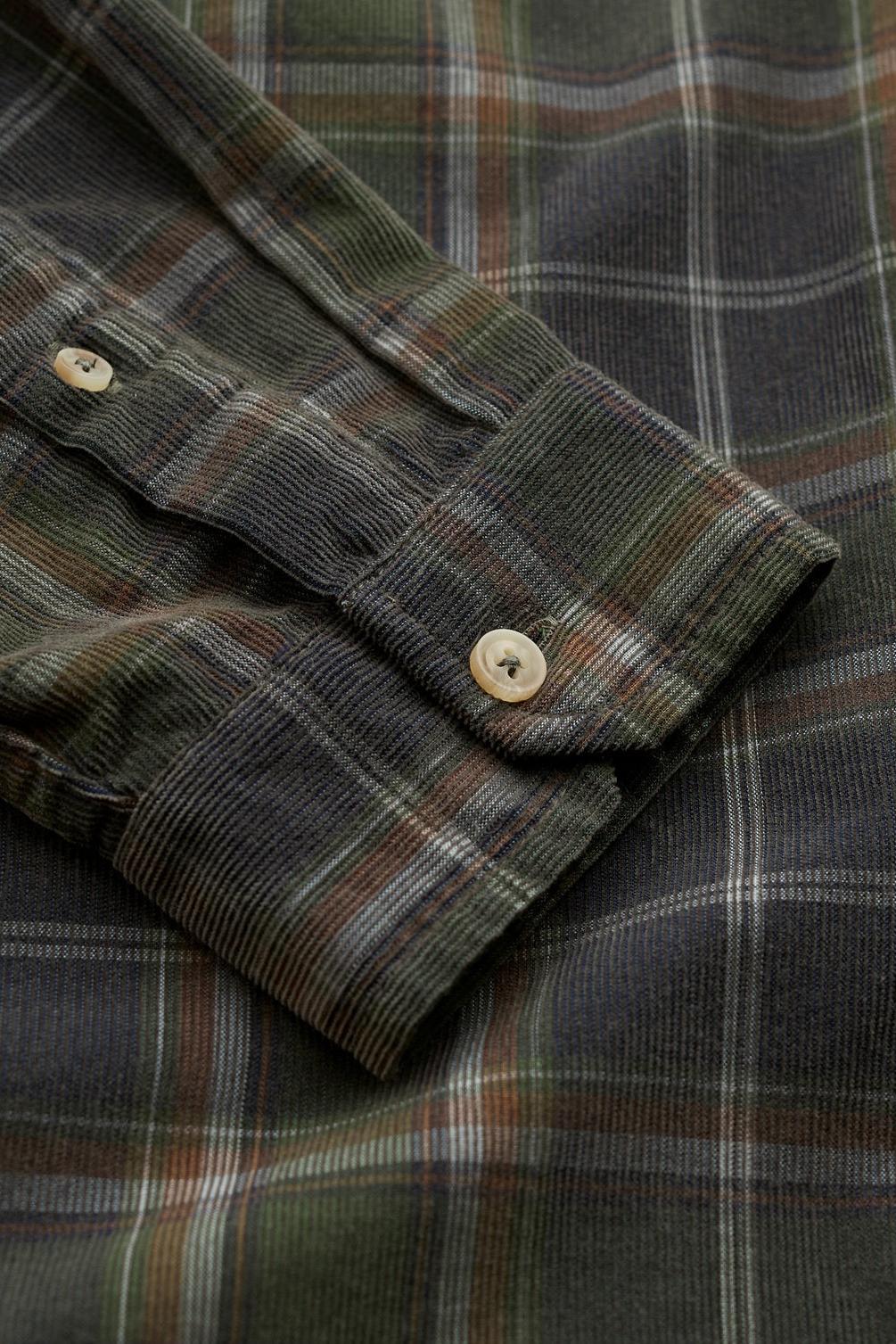 Close-up of a plaid button-up shirt sleeve with a buttoned cuff, showing a dark green, brown, and gray tartan pattern with light tan buttons.
