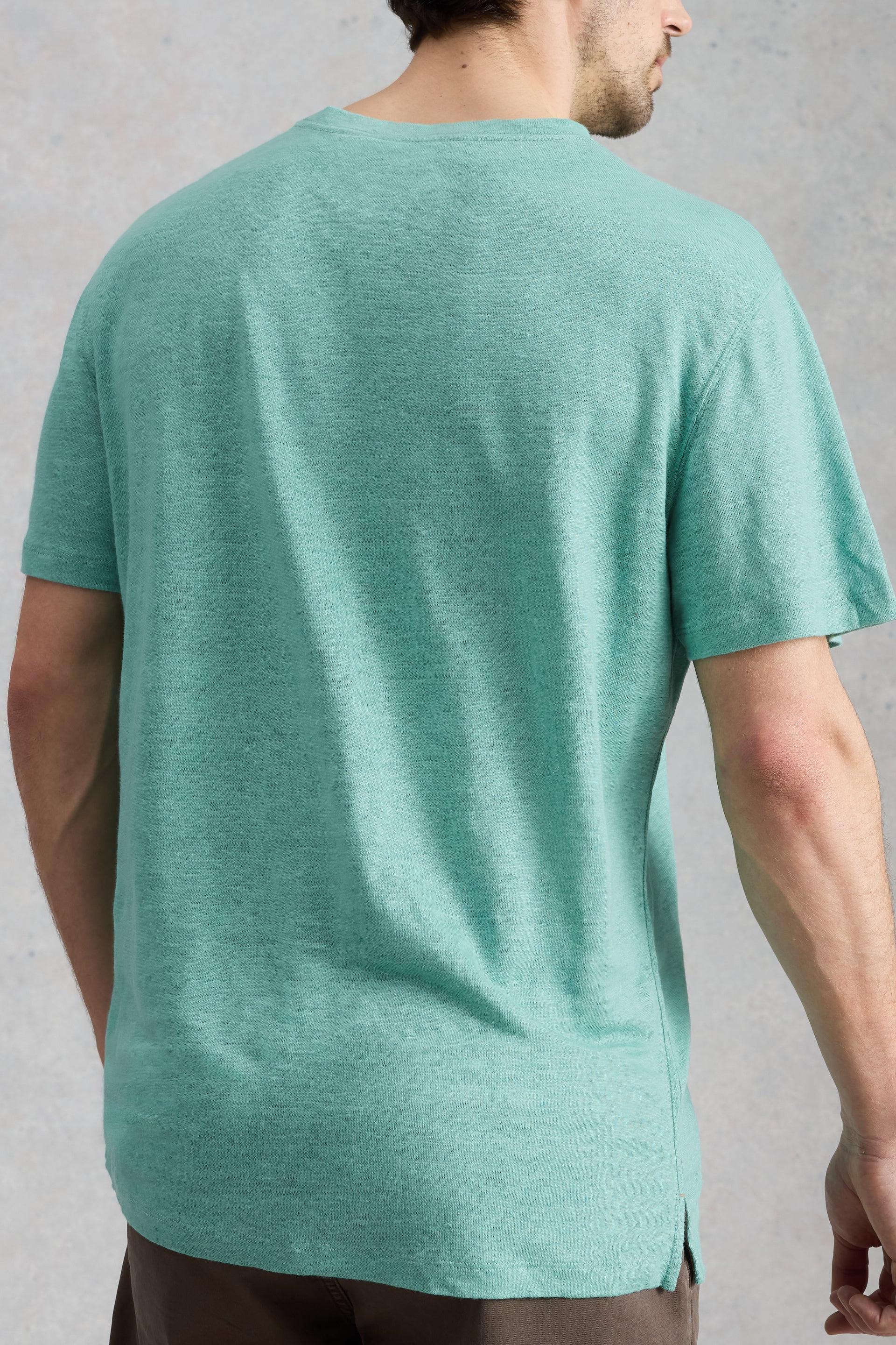 A man wearing a green mens linen t-shirt seen from the back, available at White Stuff Ireland.