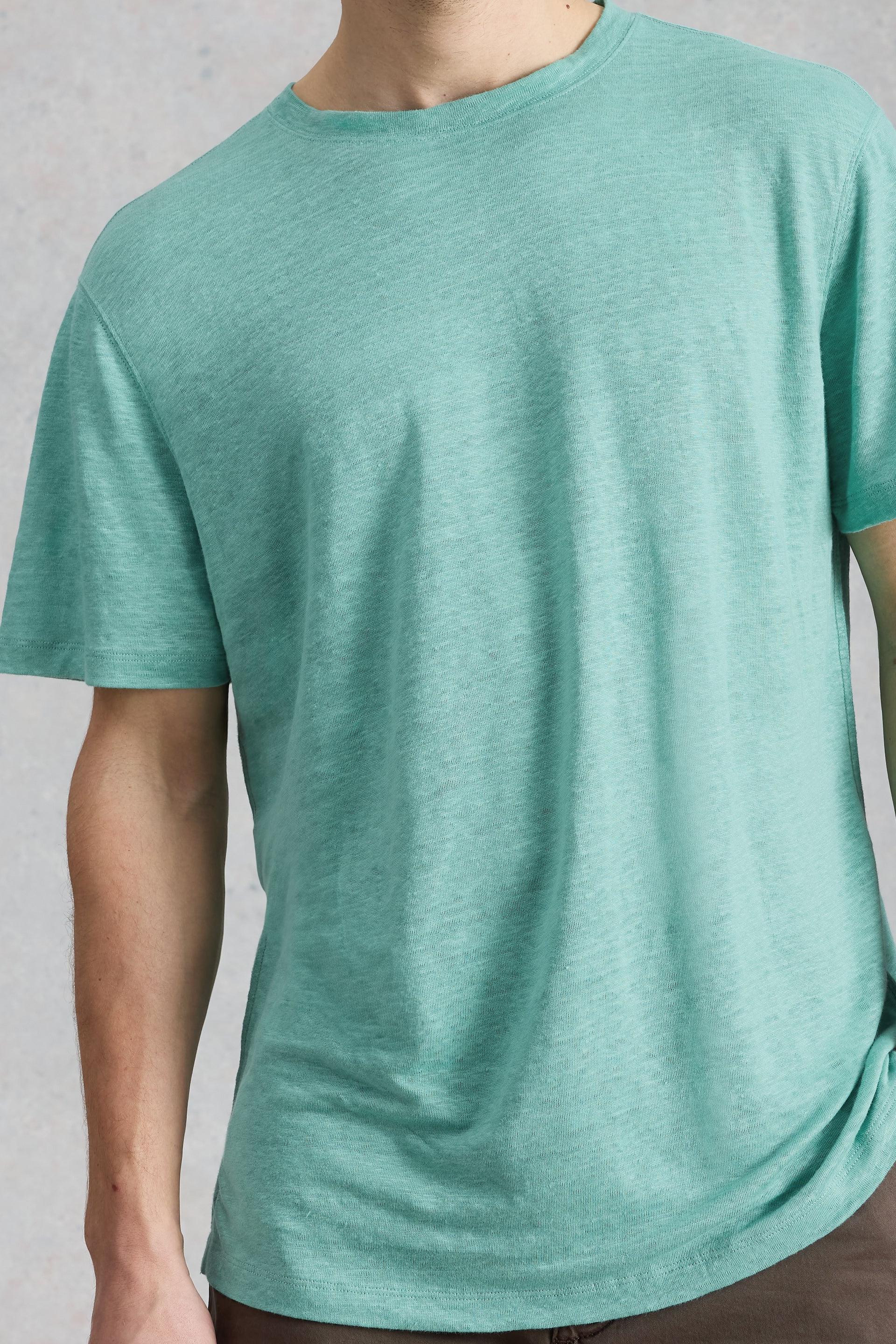 Close up of a man wearing a light green linen t-shirt from White Stuff Ireland