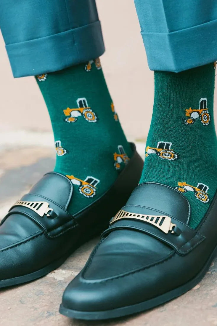 Close-up of a person wearing black leather loafers with green socks featuring a tractor pattern.