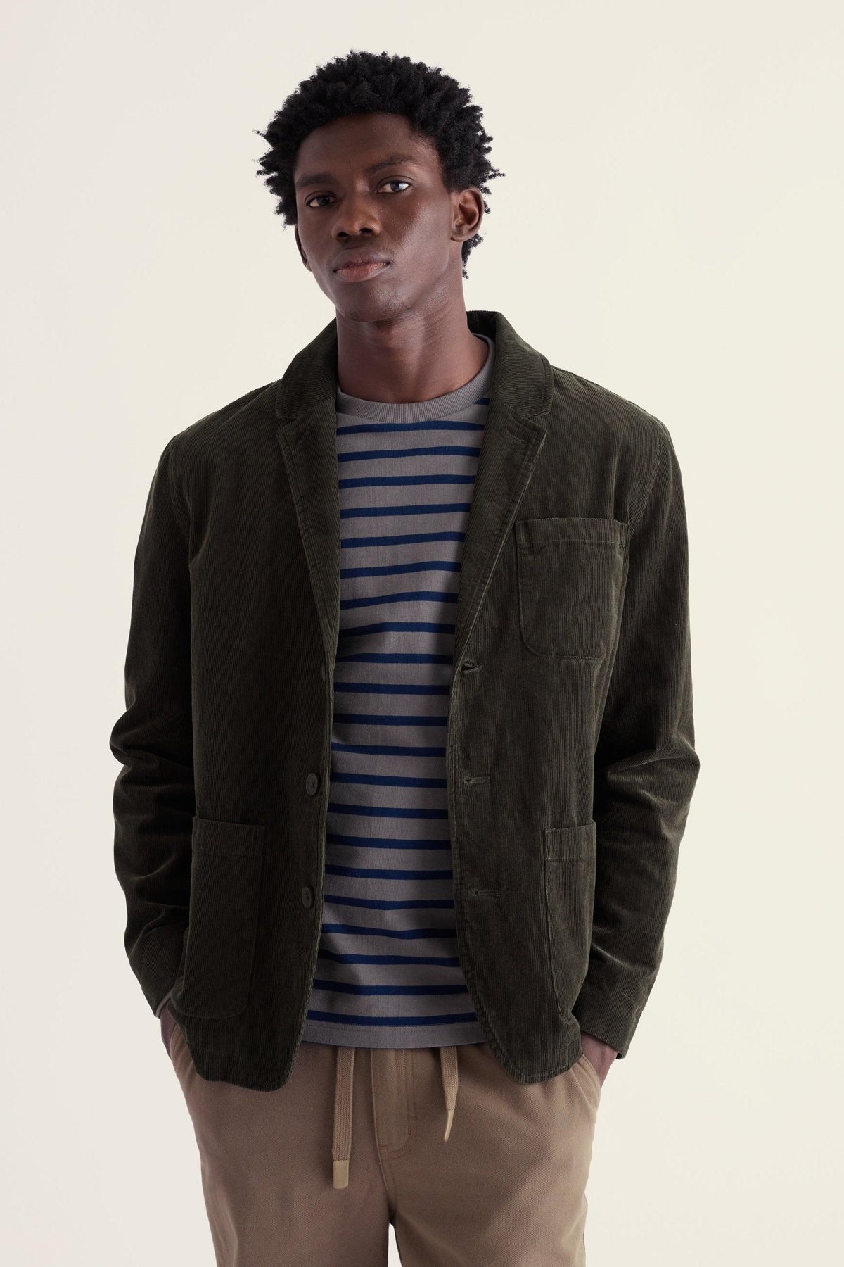 A man wearing an olive green organic cotton corduroy blazer over a striped t-shirt against a light background.