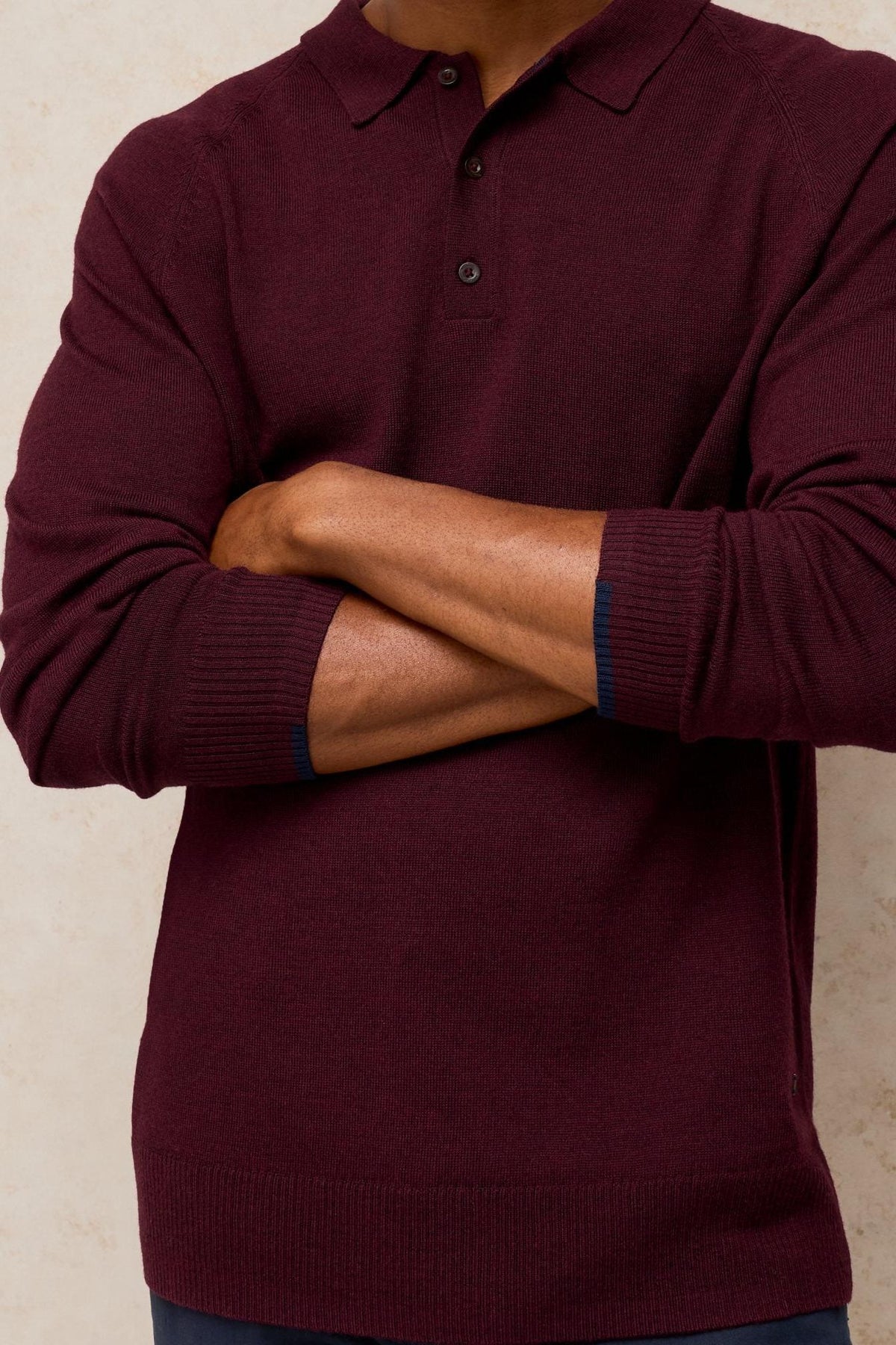 A man wearing a long-sleeved plum-coloured merino wool polo shirt with arms crossed against a neutral background.
