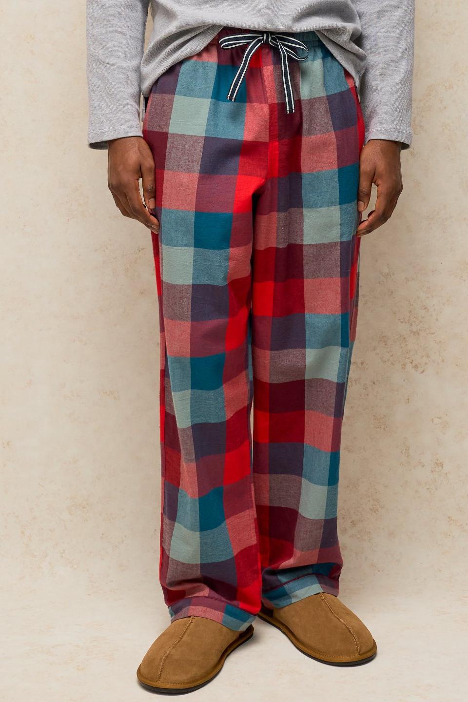 A person wearing red check organic cotton pyjama trousers and brown slippers.