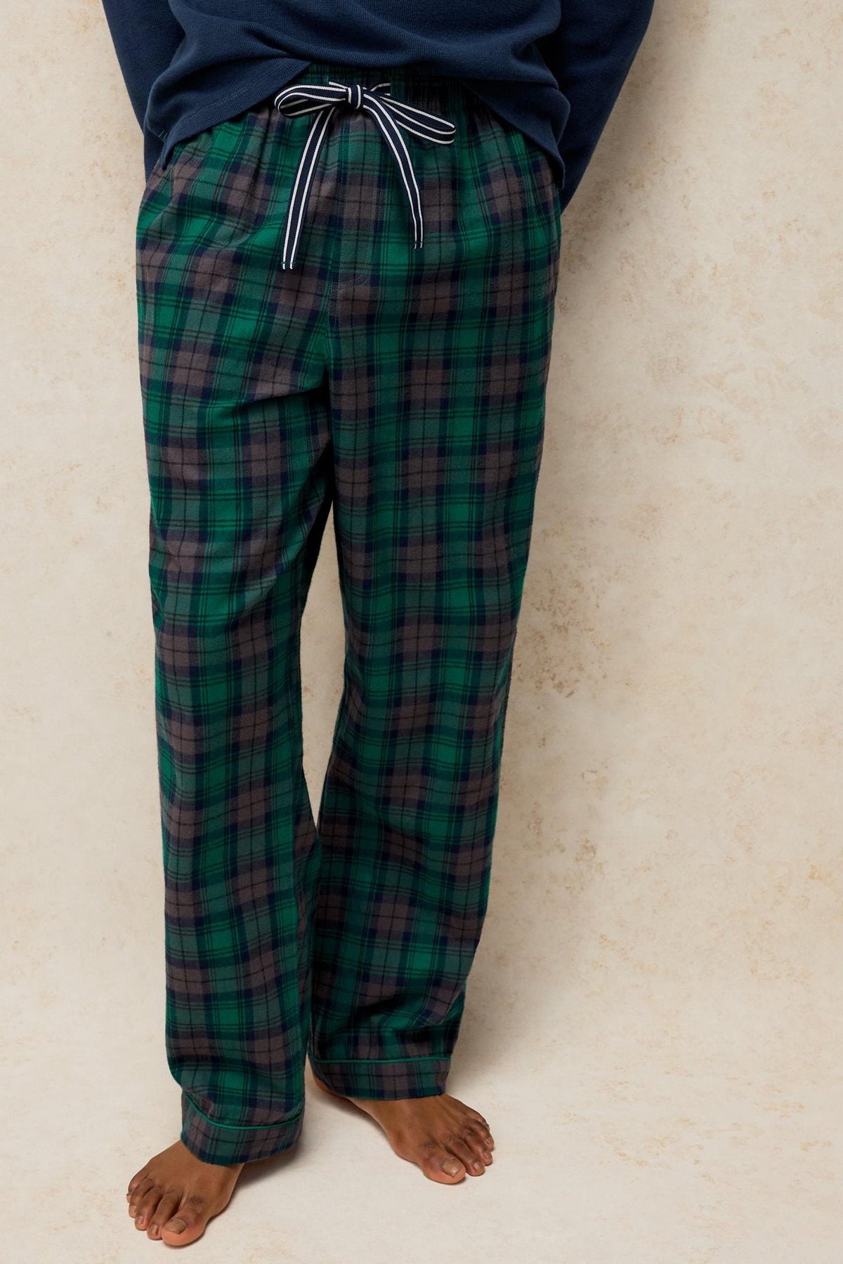 Man wearing green tartan cotton pyjama bottoms with a drawstring waist against a neutral background.