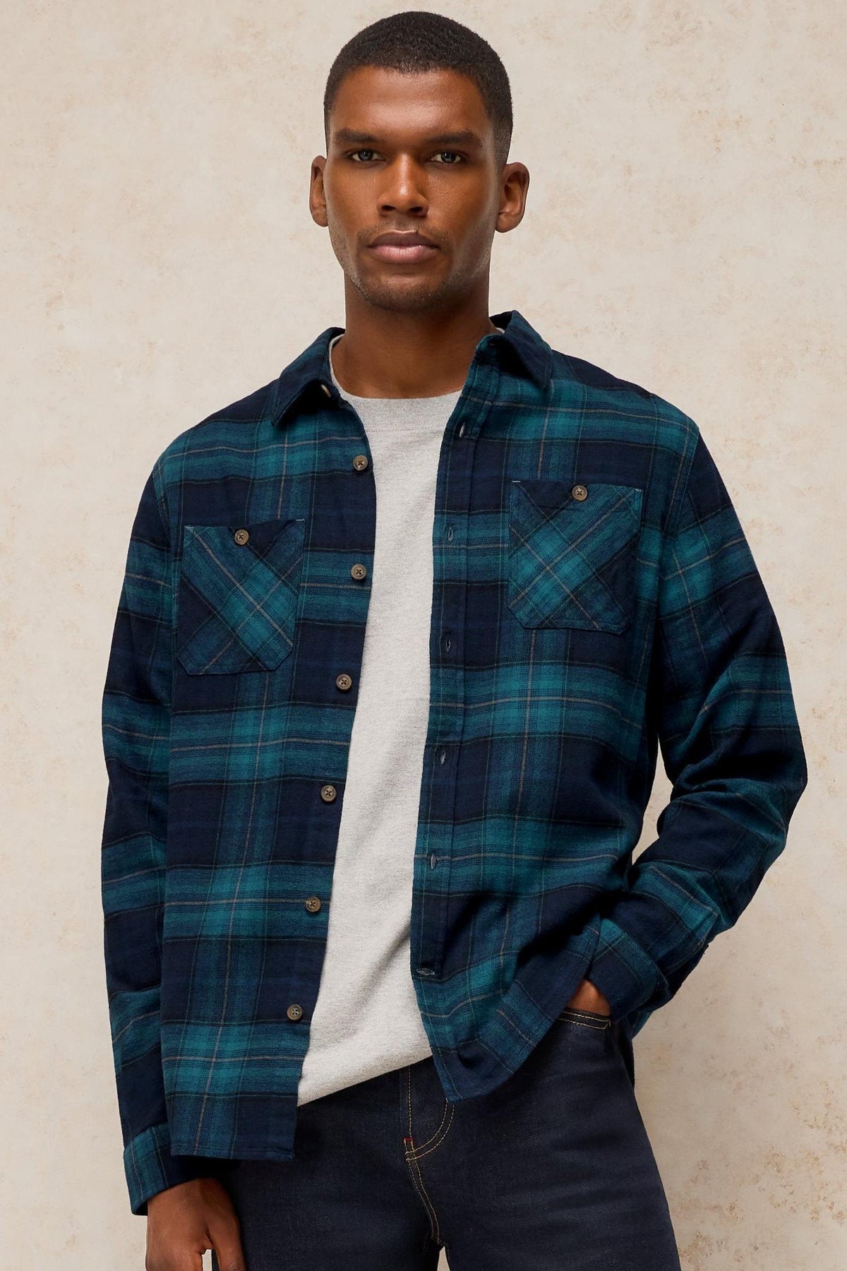 A man wearing a teal and blue plaid long sleeve organic cotton shirt over a grey t-shirt.