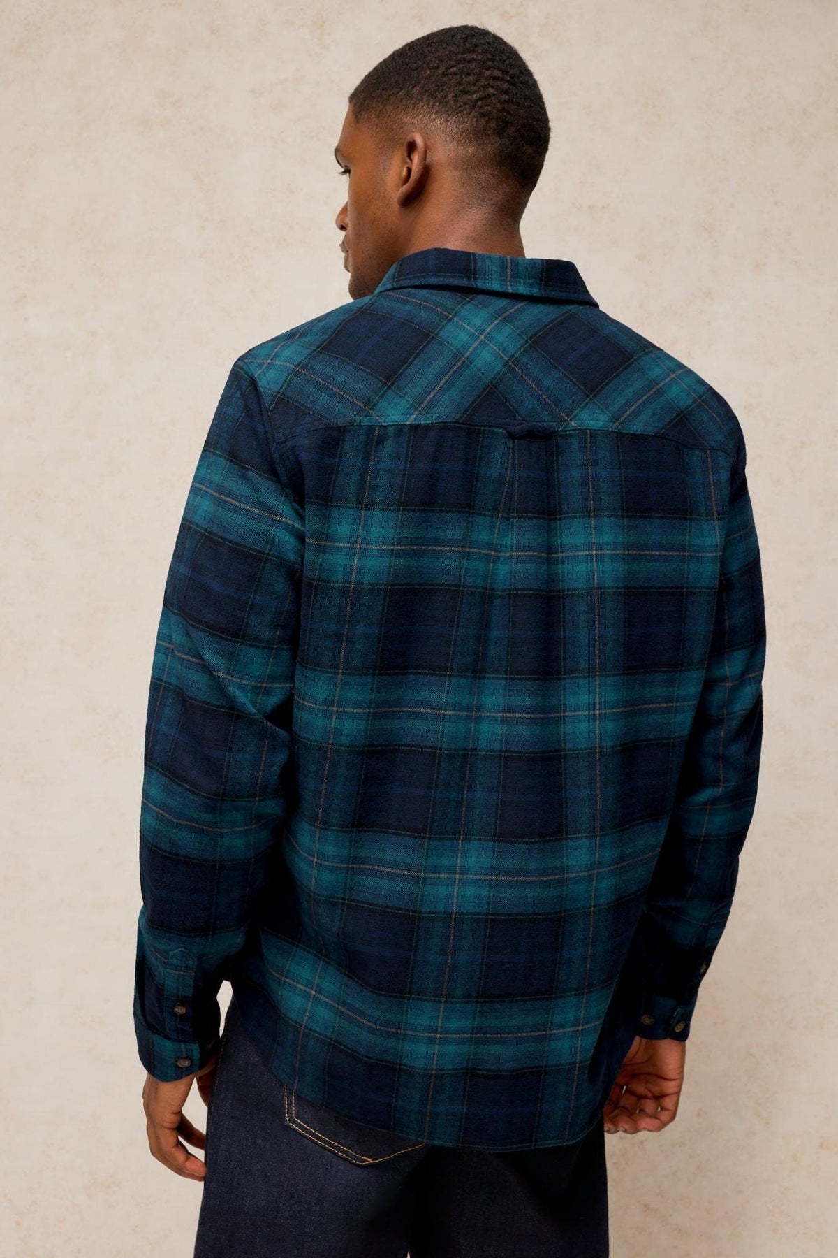 A man wearing a long sleeve teal and blue plaid organic cotton shirt seen from the back.