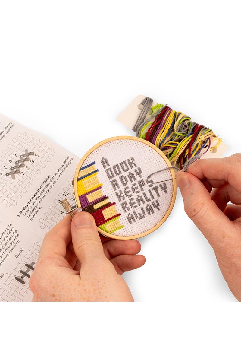 A miniature hand stitch with the detail "A book a day keeps reality away"