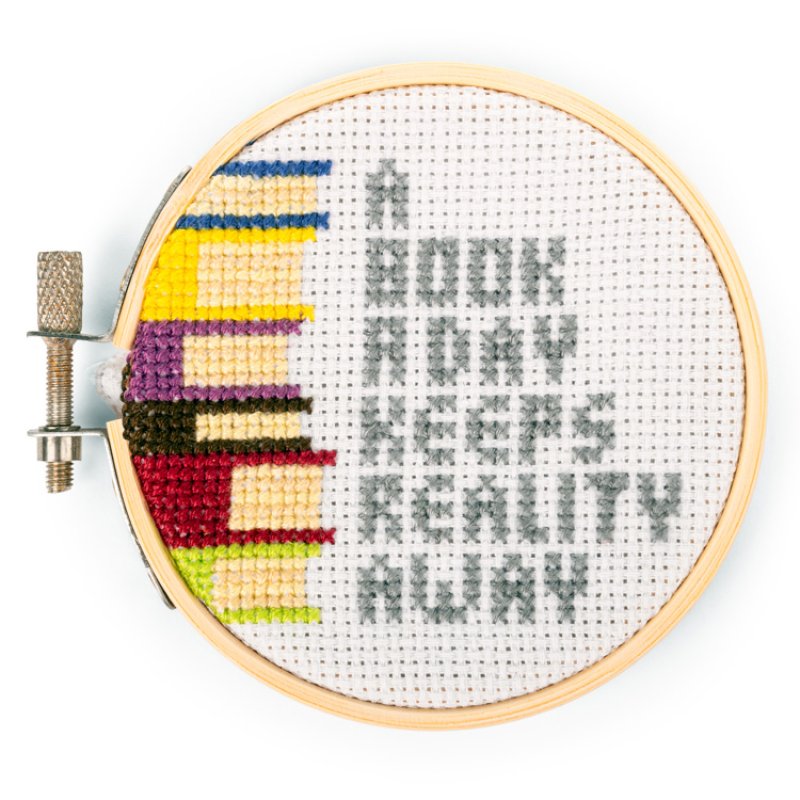 Cross-stitched hoop with 'A book a day keeps reality away' text and colorful book illustrations.