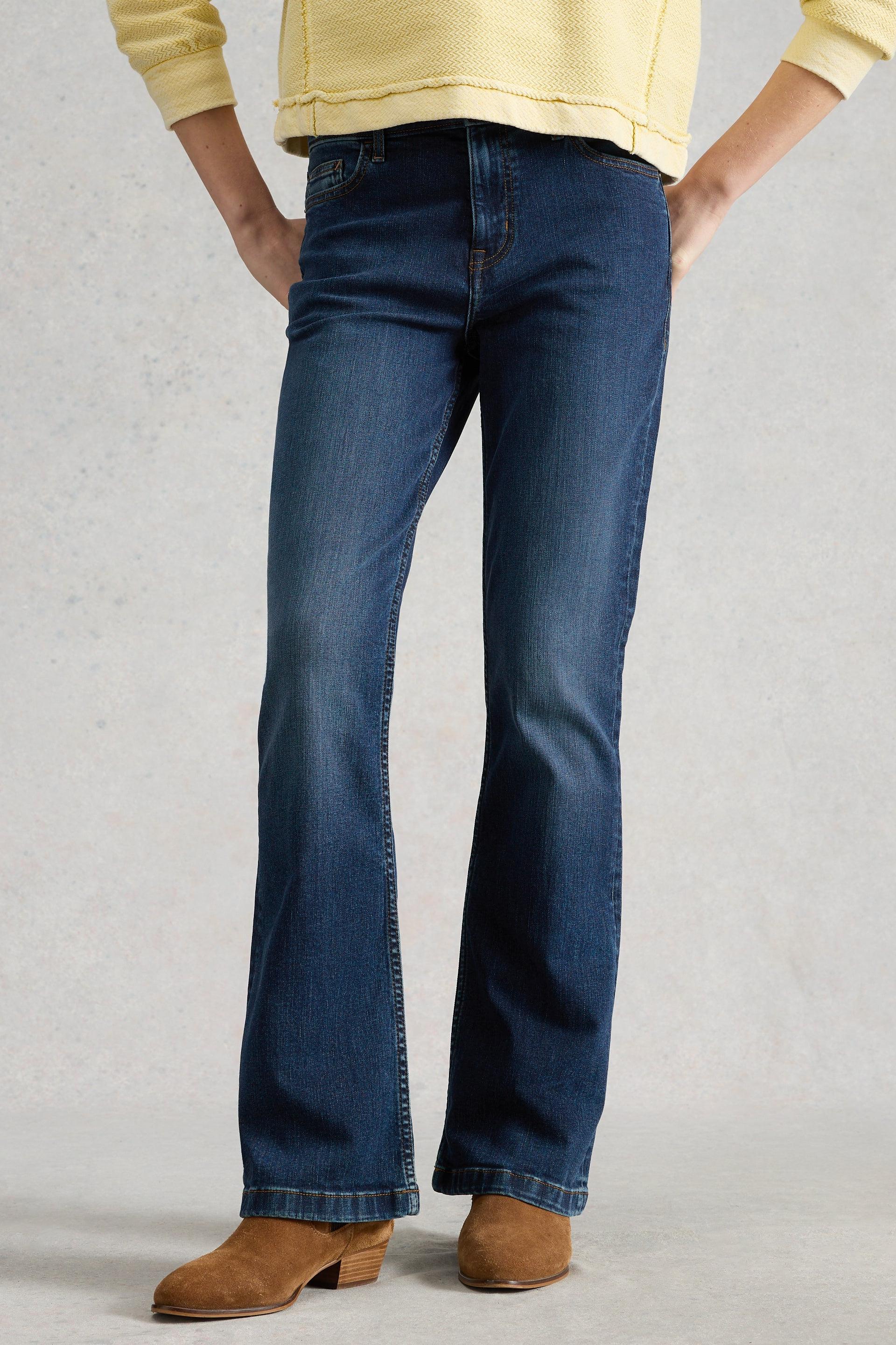 A model wearing dark blue bootcut jeans and a yellow sweater against a neutral background.