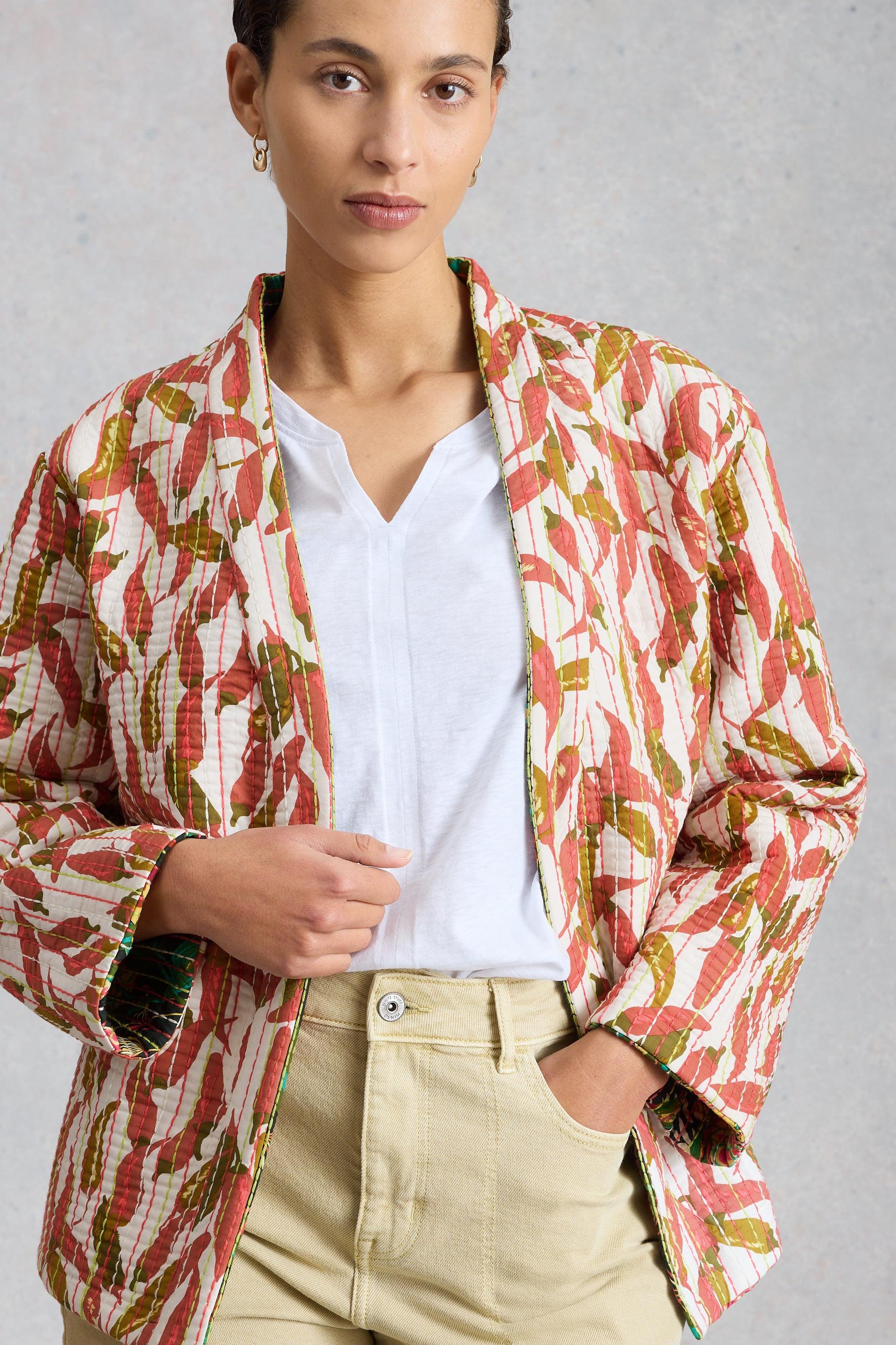 A model posing in a white tee and a floral print quilted organic cotton jacket against a grey background.