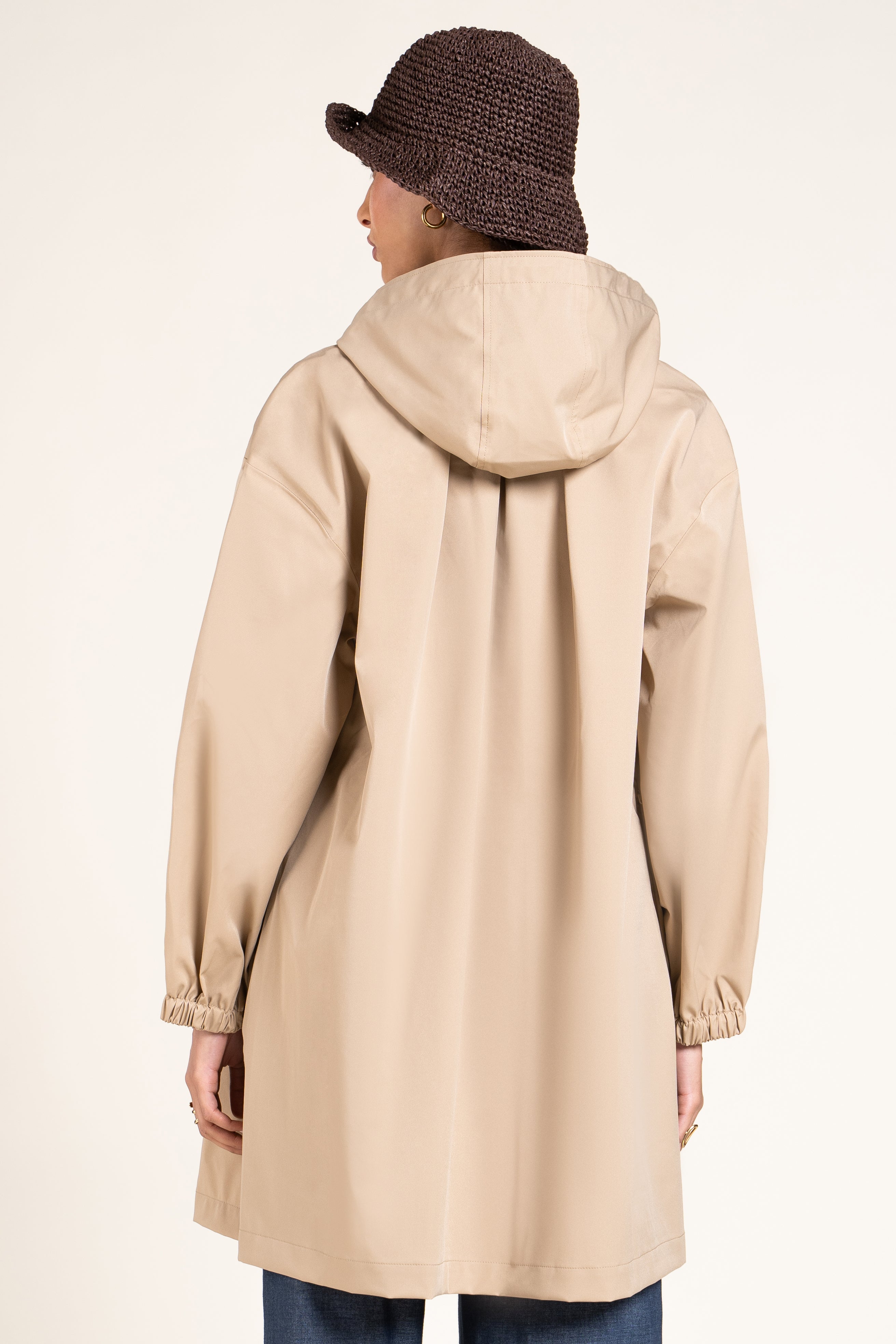 Back view of a person wearing a beige Flotte waterproof coat and a brown woven bucket hat.