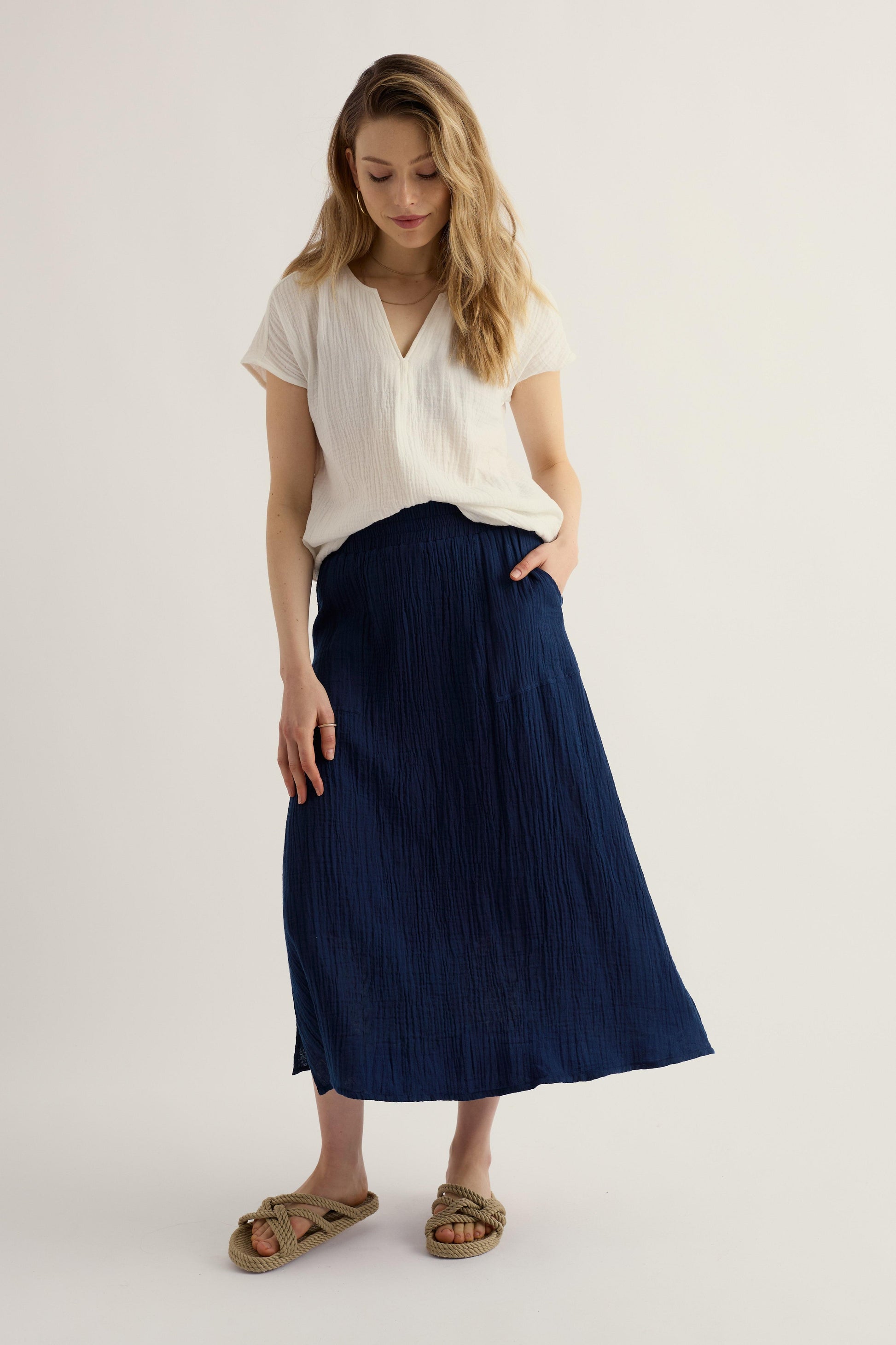 Woman wearing a white top and navy skirt on a plain background