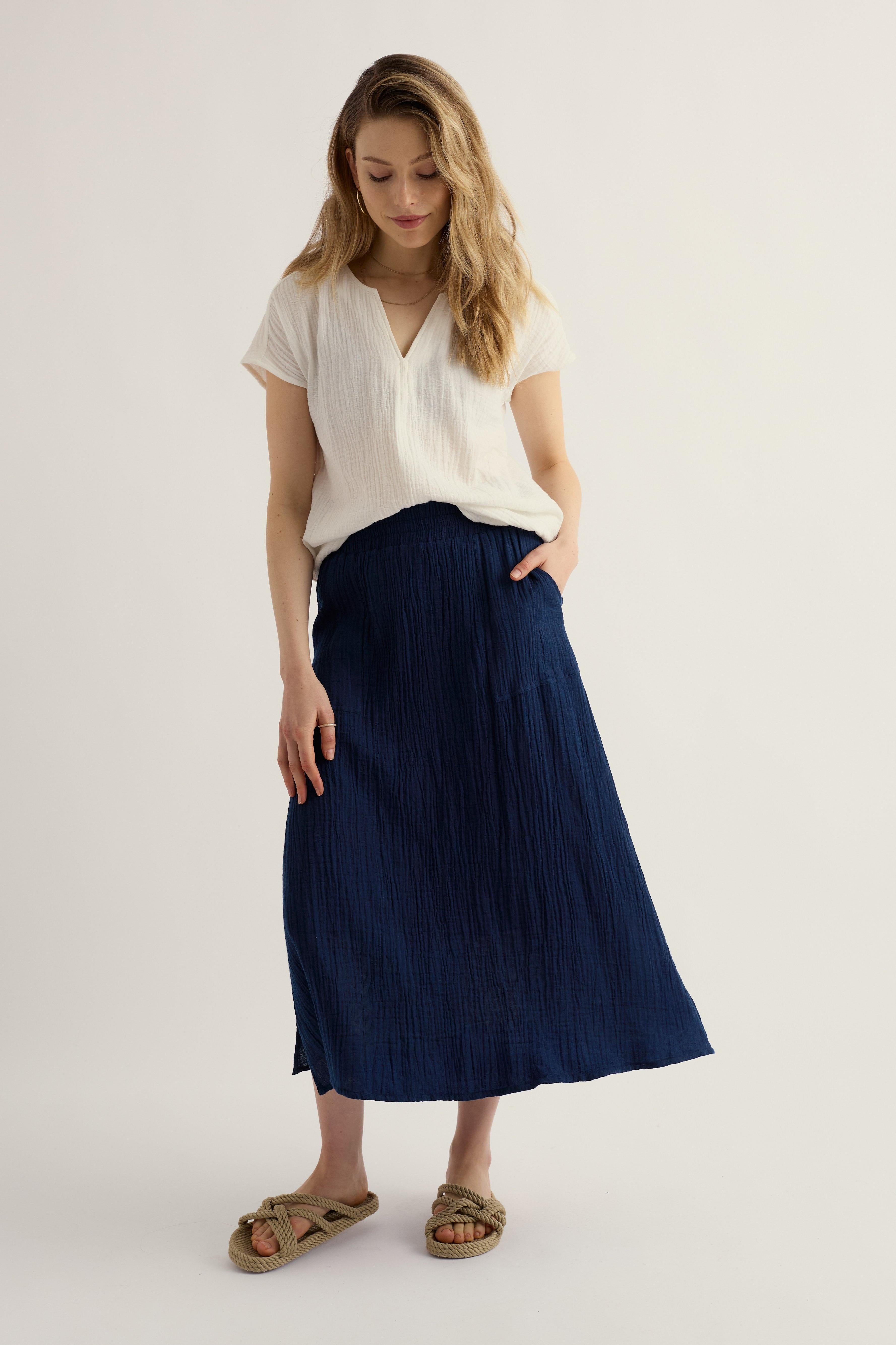 Woman wearing a white top and navy skirt on a plain background