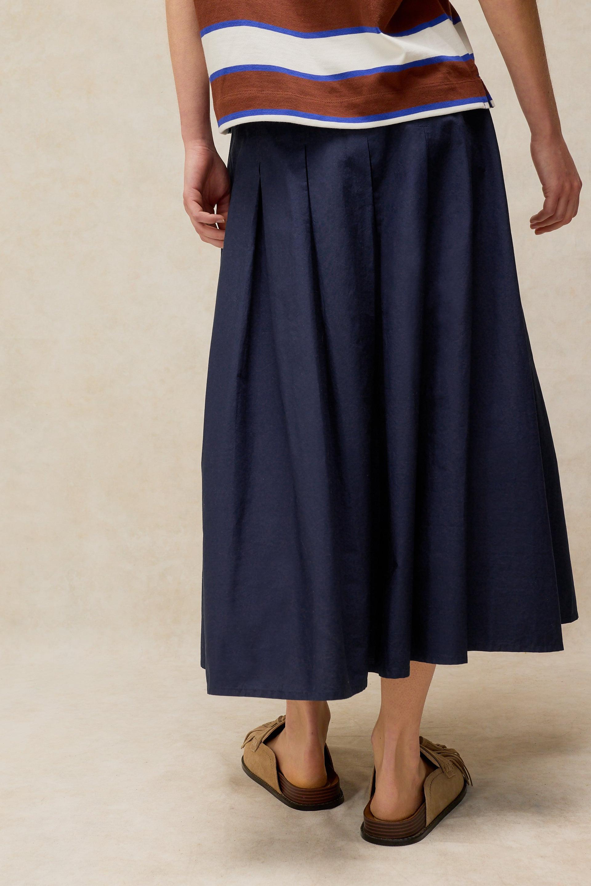 Person wearing a navy blue skirt with a striped shirt on a beige background