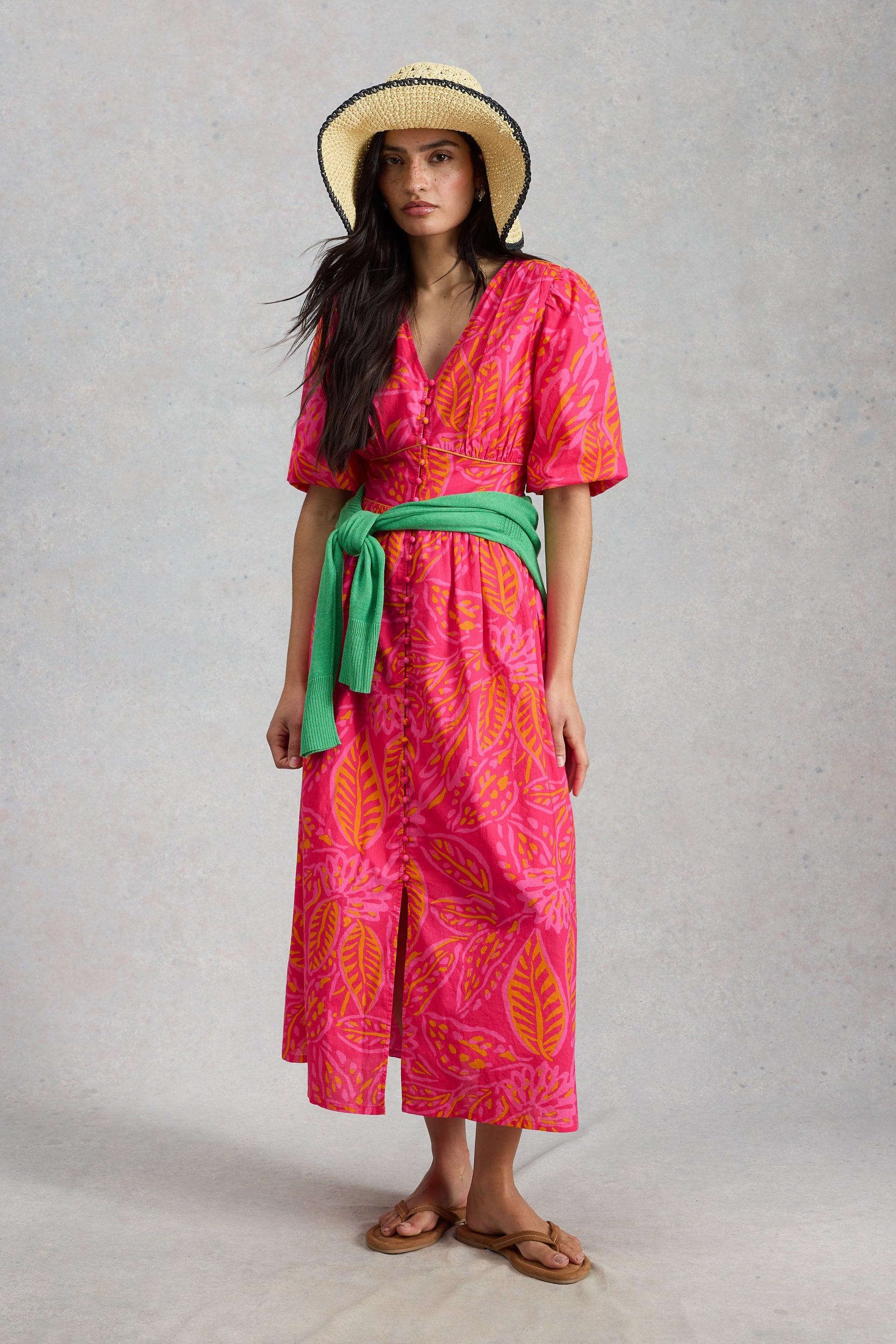 Woman wearing a bright pink printed organic cotton midi dress and a straw hat.
