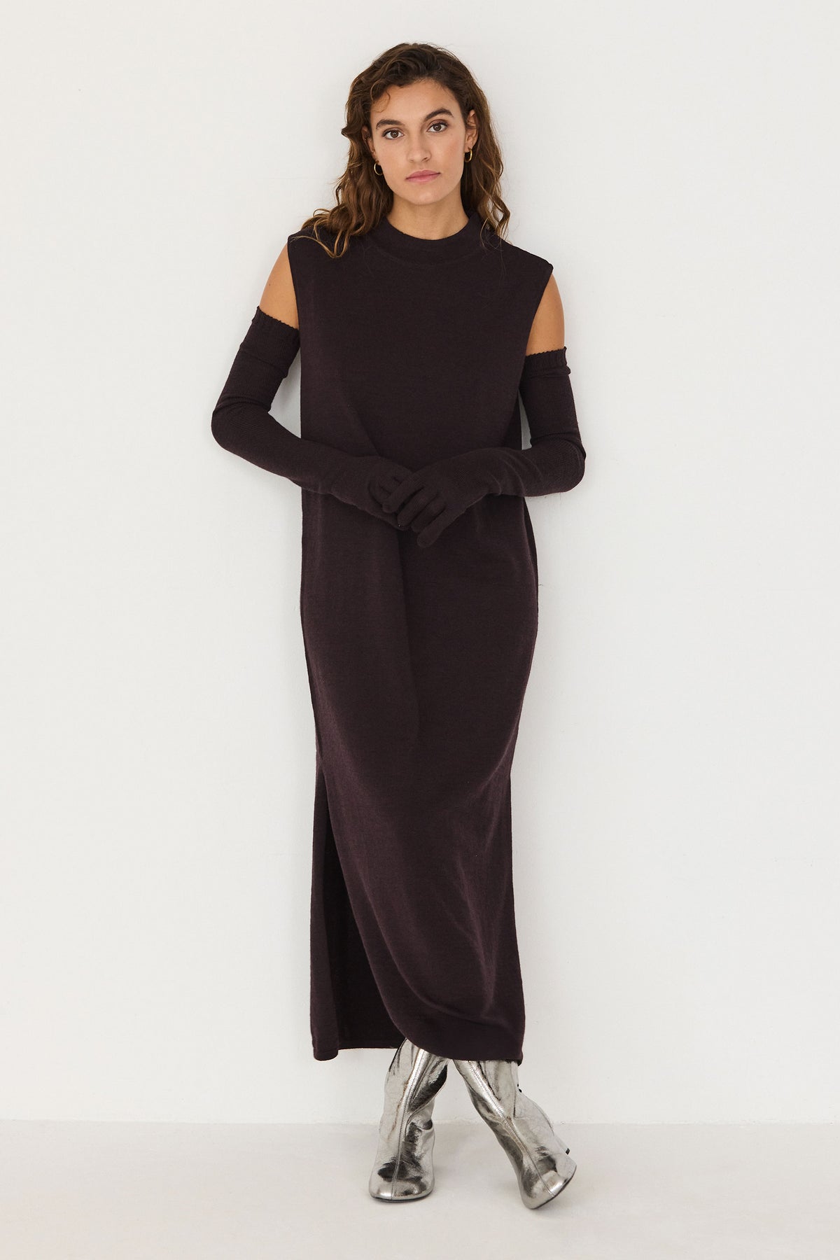 A woman wearing a dark brown sleeveless dress with matching full-length wool gloves against a white background.