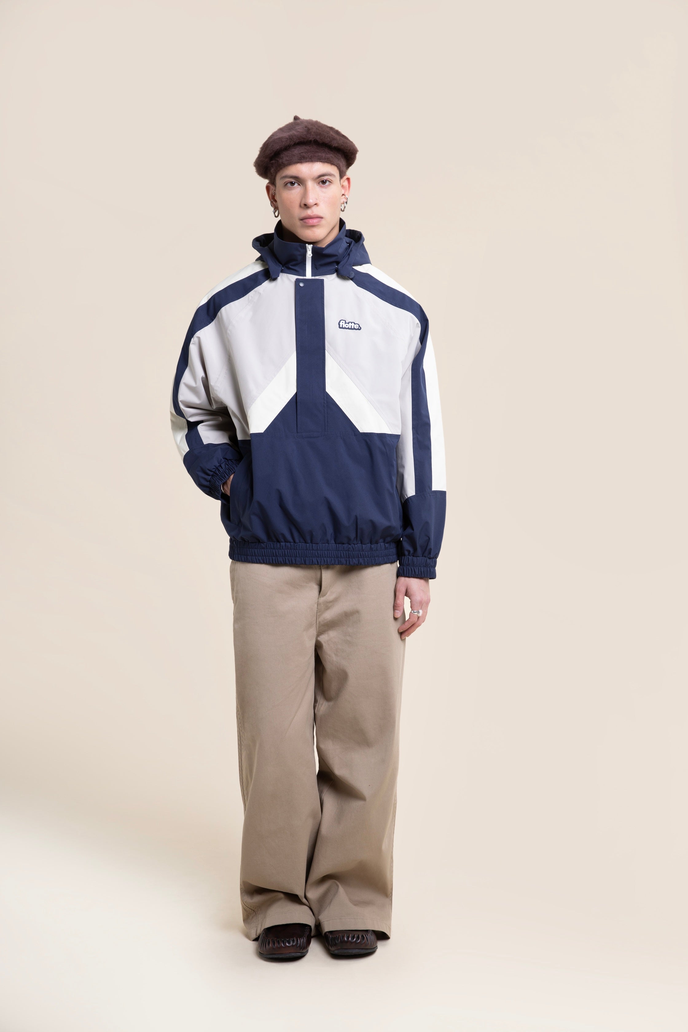 A person posing in a navy and white waterproof jacket and brown beret against a light background.