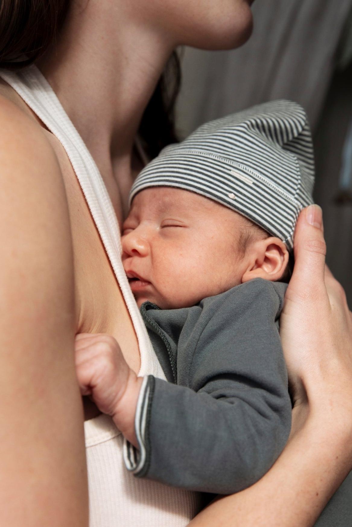 Newborn baby wearing a striped hat being held by an adult