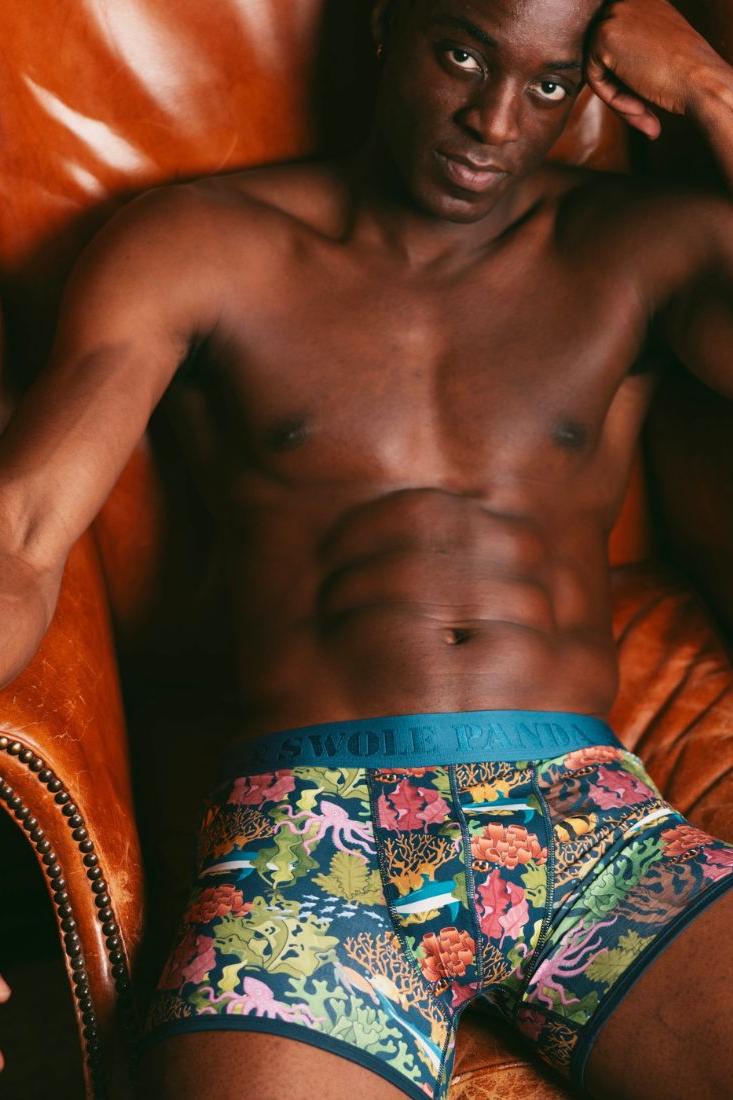 Muscular man wearing floral print bamboo fiber boxer briefs sitting in a brown leather armchair.