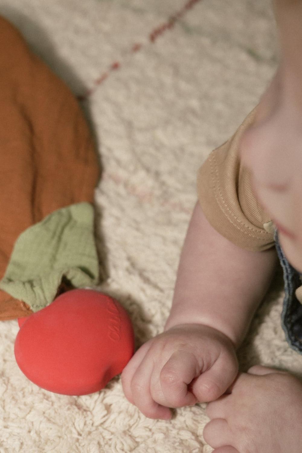 Baby's hand reaching towards a 100% natural rubber doudou on a textured surface