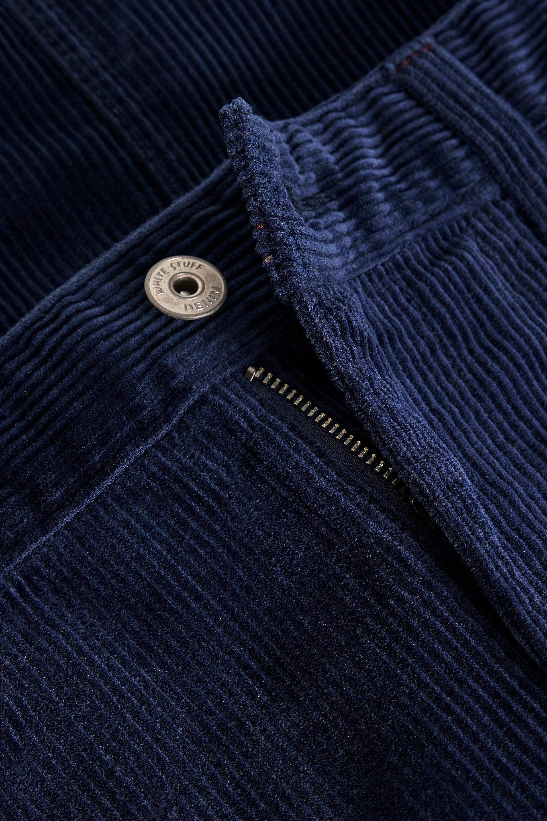 Close-up of dark navy corduroy skirt showing the ribbed texture, a metal snap button, and a zipper.