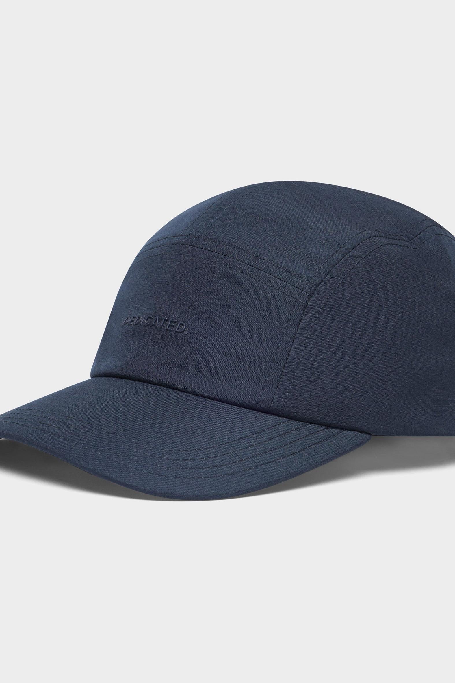 A dark navy blue five-panel cap with a curved brim, featuring a subtle tonal embroidered logo on the front, set against a light gray background.